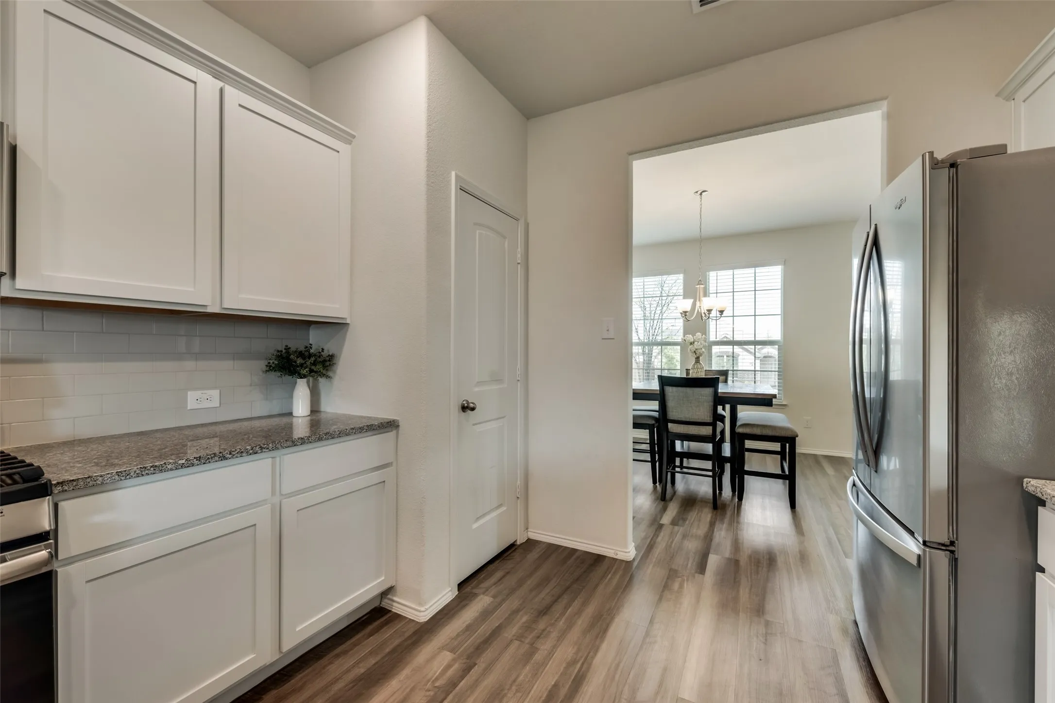 Kitchen featuring granite countertops, a subway tile backsplash, white shaker-style cabinetry, and wood-finish flooring
