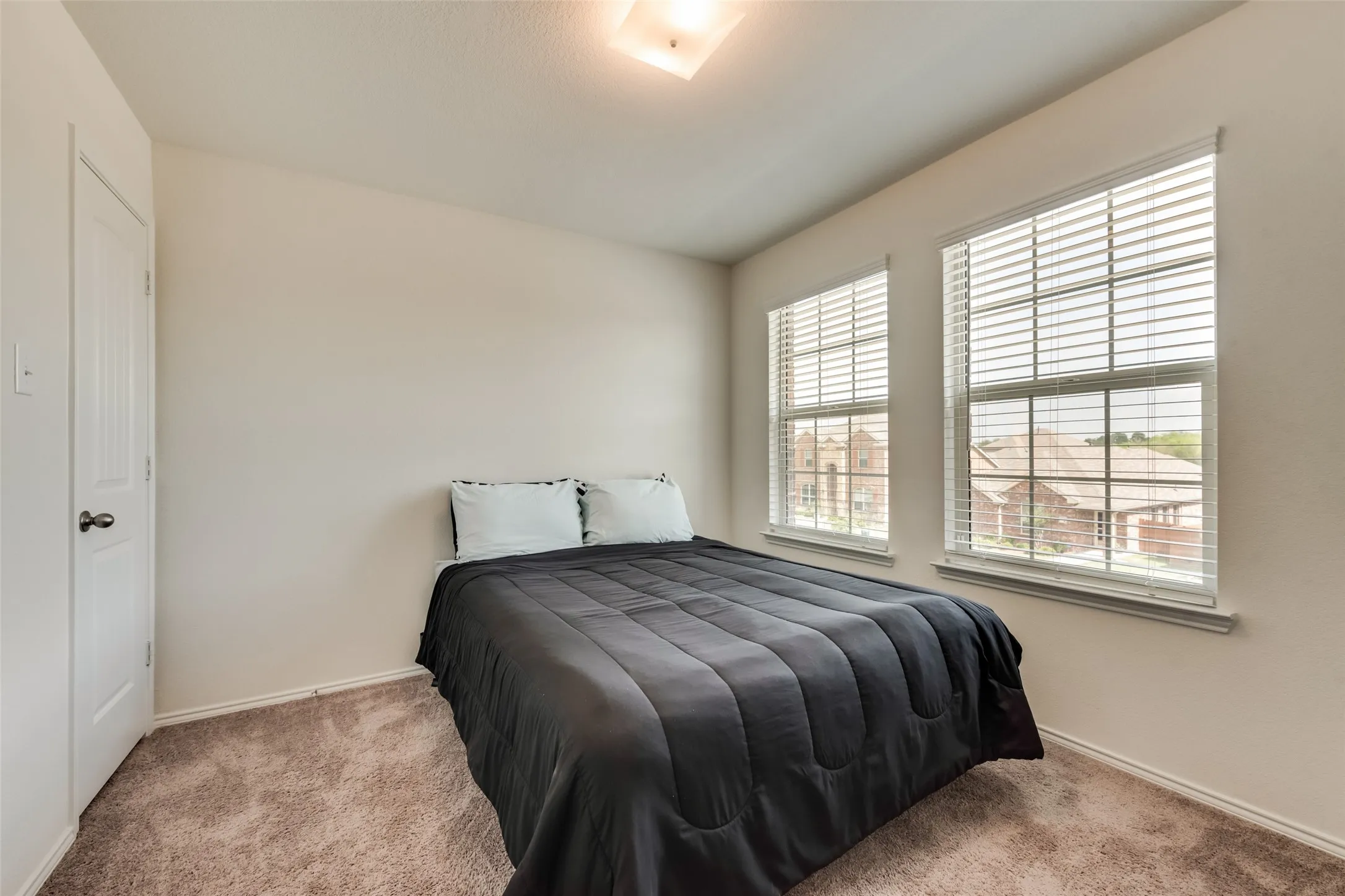 Bedroom featuring two windows with horizontal blinds, neutral wall paint, and textured carpet flooring