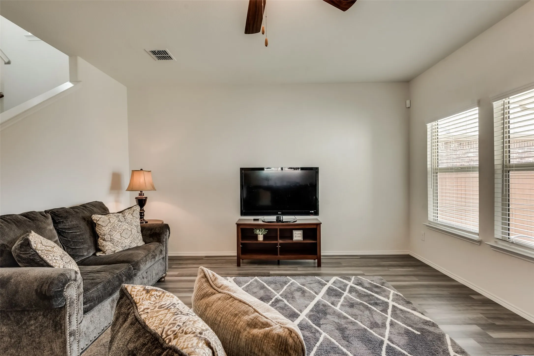 Living area featuring wood-finish flooring, white walls, and multiple windows with blinds
