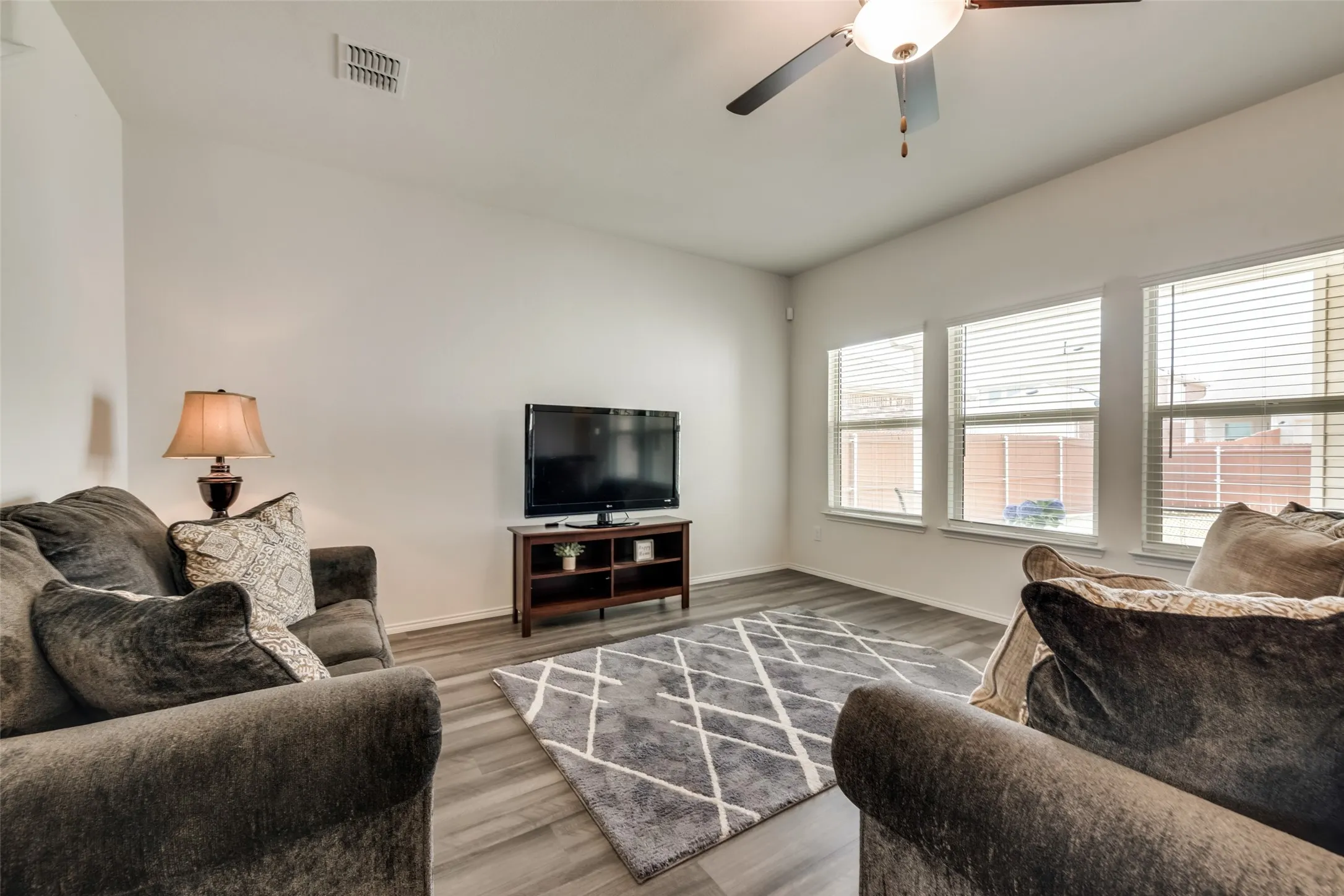 Living area featuring wood-finish flooring, white walls, and a ceiling fan with integrated lighting