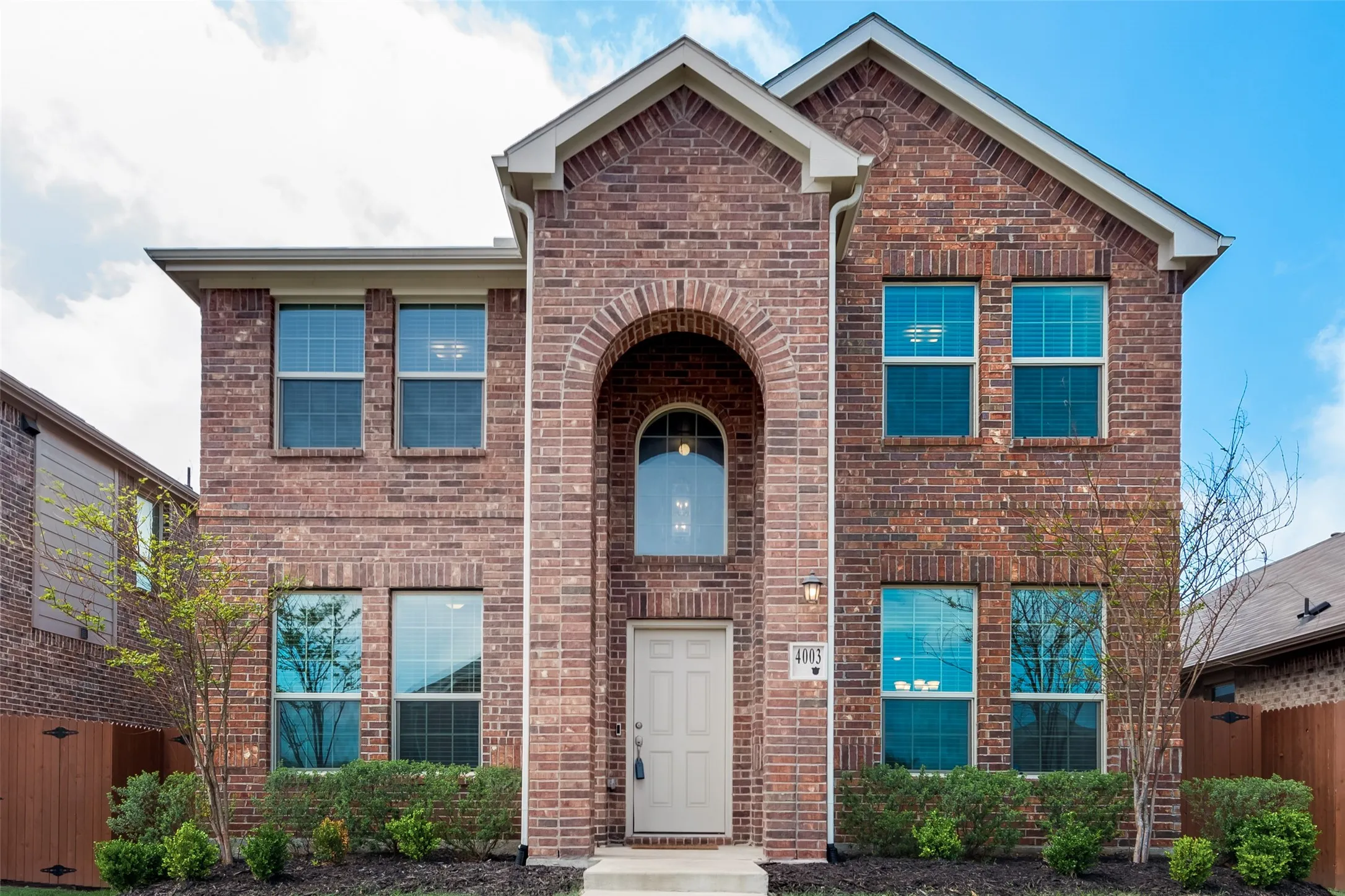 Two-story brick exterior featuring an arched entryway, multiple windows with grid detailing, and a light-colored front door