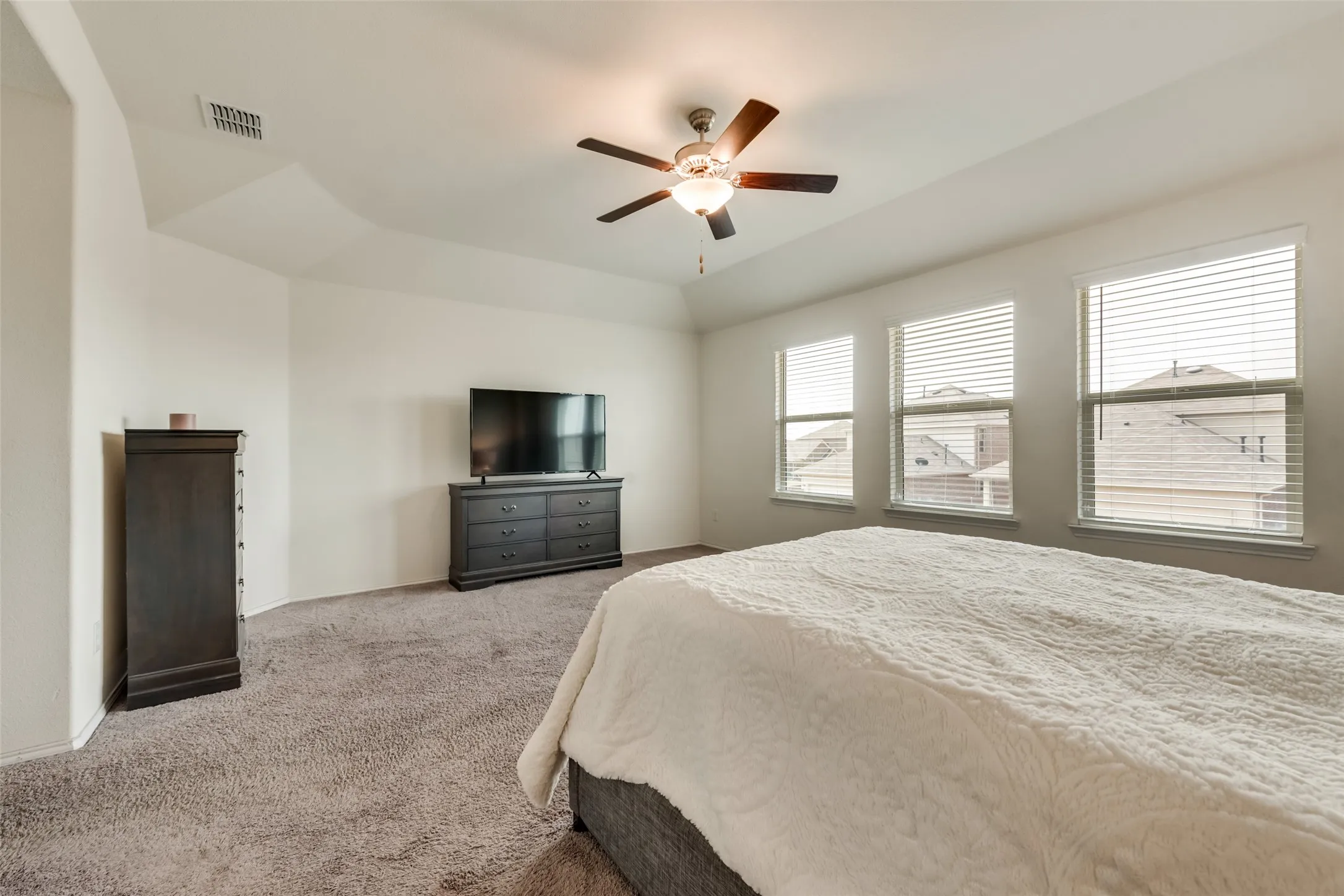 Carpeted bedroom featuring a tray ceiling, ceiling fan with integrated lighting, and three large windows with horizontal blinds