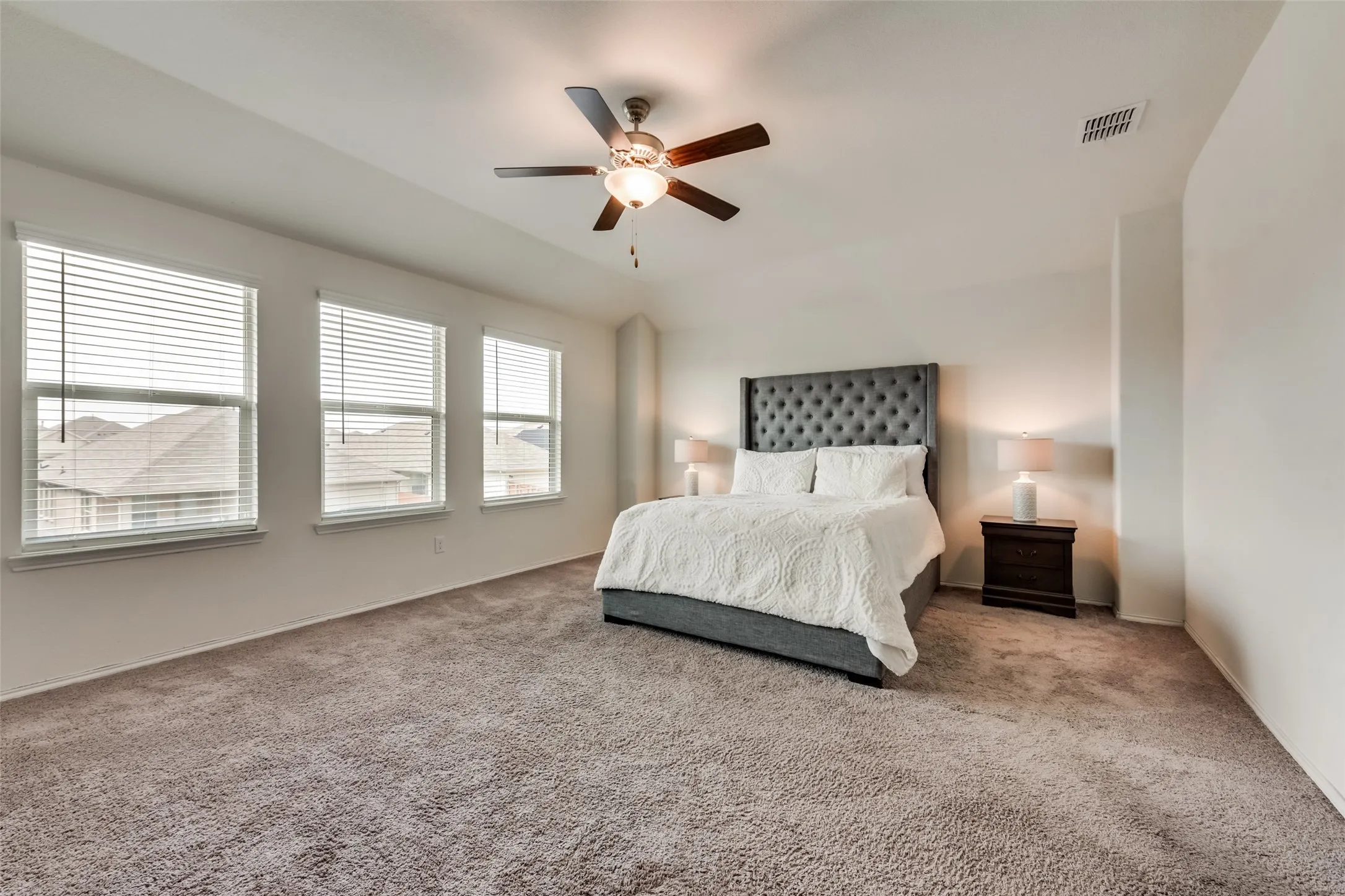 Spacious room featuring three windows with blinds, a ceiling fan with light fixture, and neutral carpeting