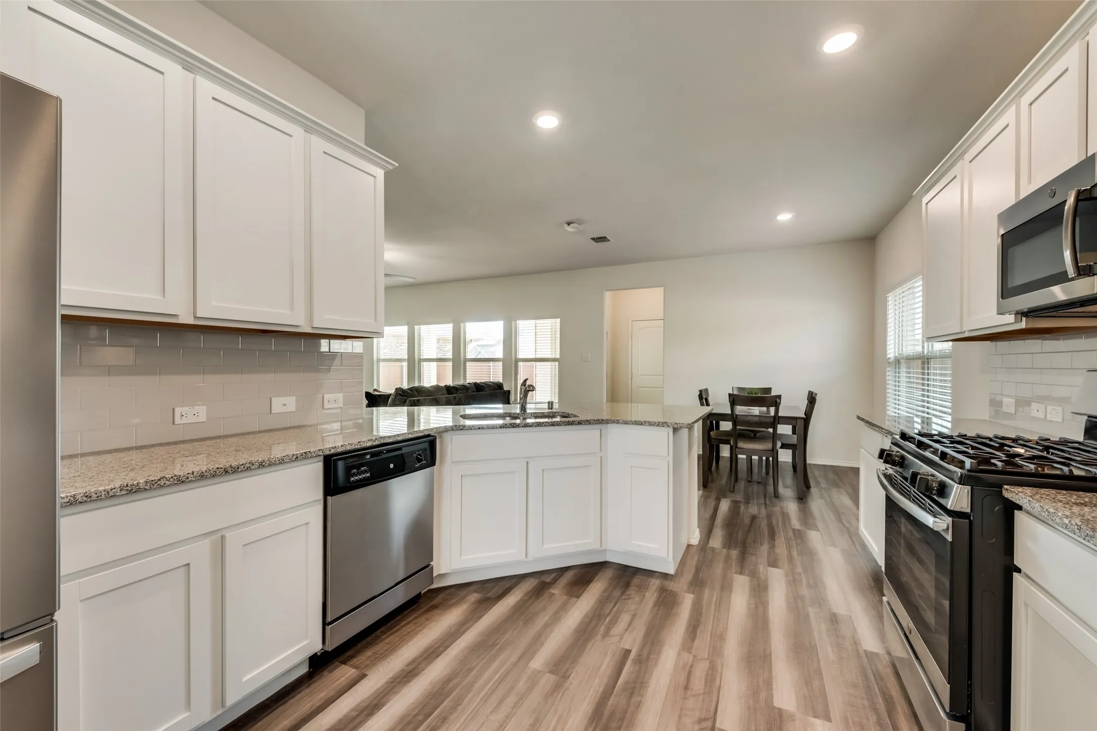 Contemporary kitchen featuring wood-finish flooring, white cabinetry, granite countertops, and stainless steel appliances