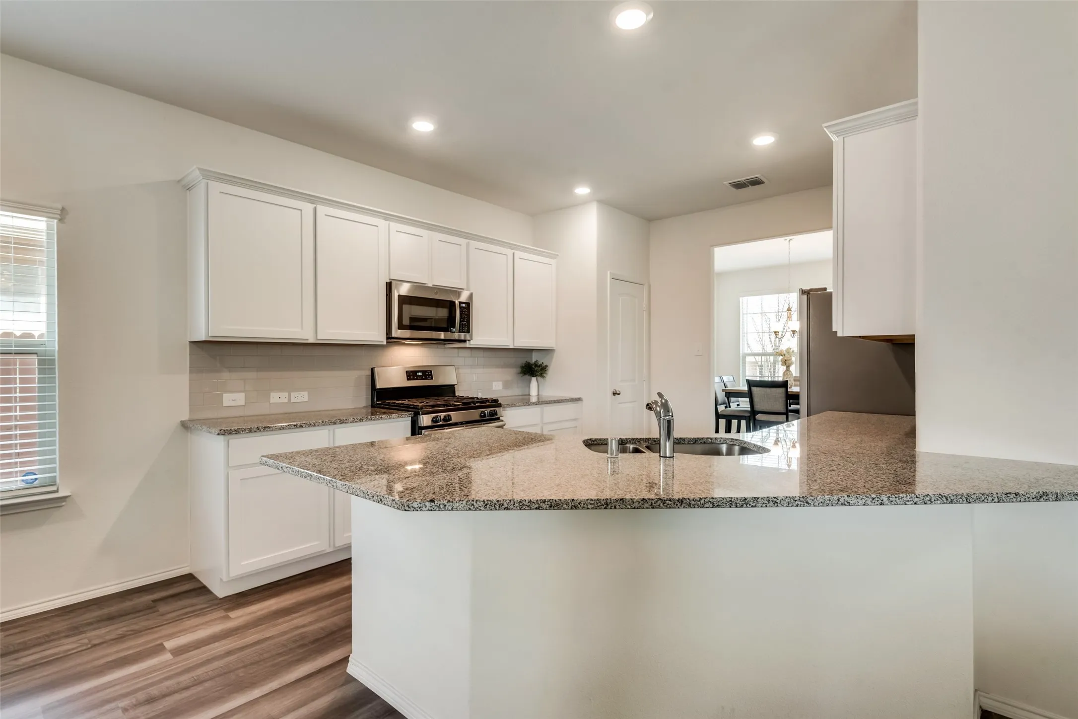 Modern kitchen featuring white cabinetry, stainless steel appliances, granite countertops, and wood-finish flooring