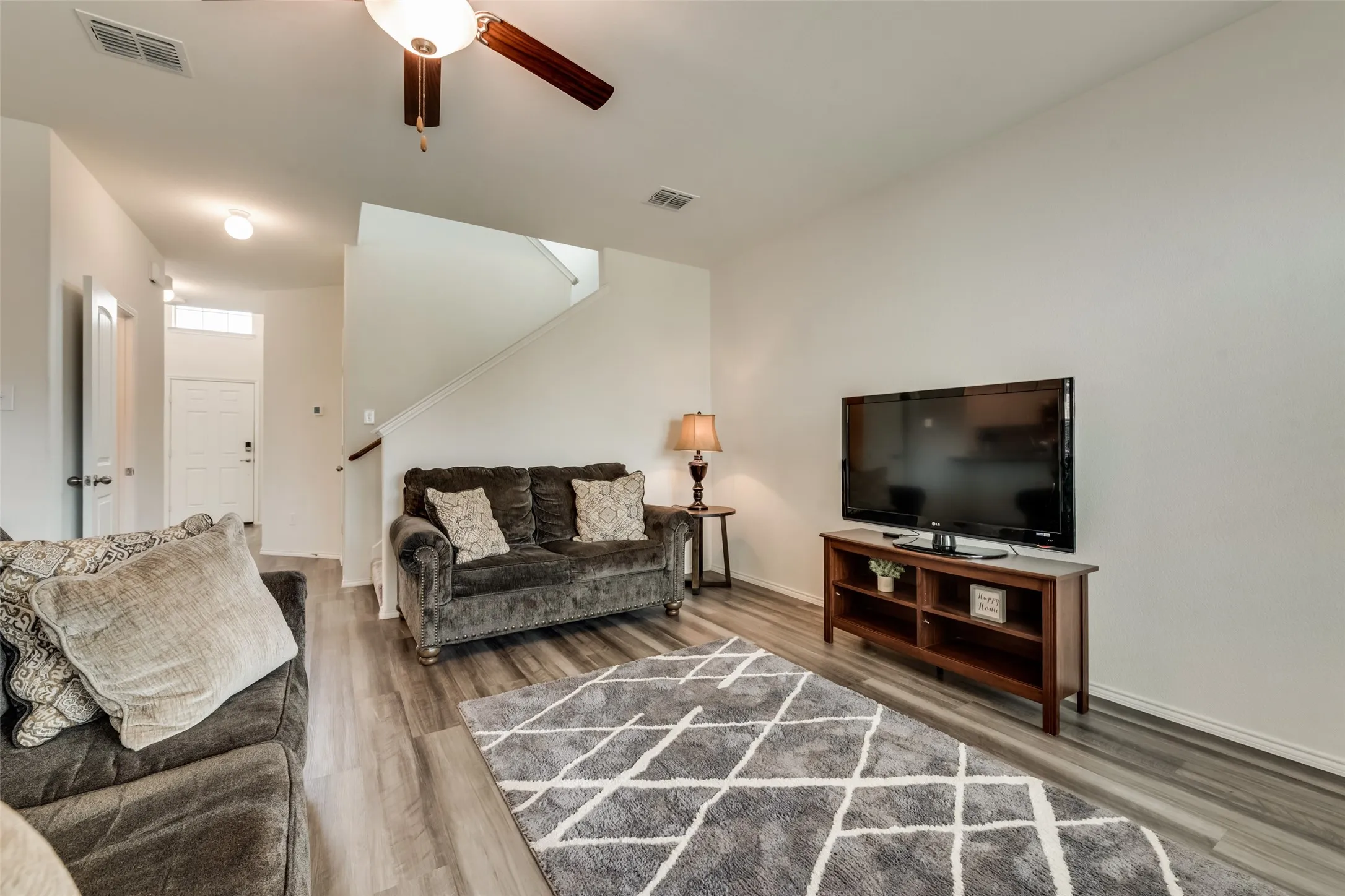 Spacious living area featuring wood-finish flooring, a neutral color palette, and a ceiling fan light fixture