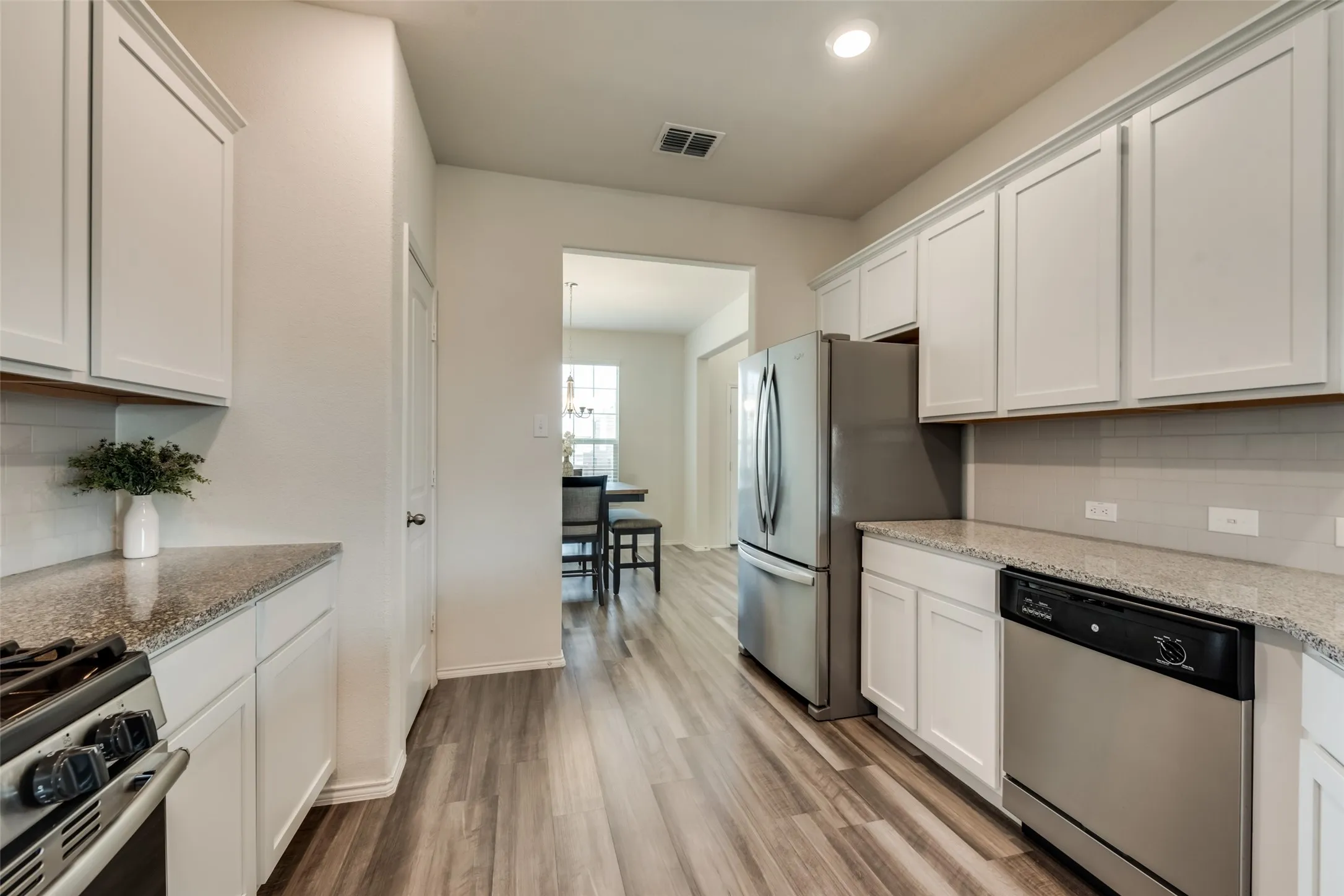 Kitchen featuring white cabinetry, gray wood-finish flooring, light-toned countertops, a stainless steel refrigerator, and a stainless steel dishwasher