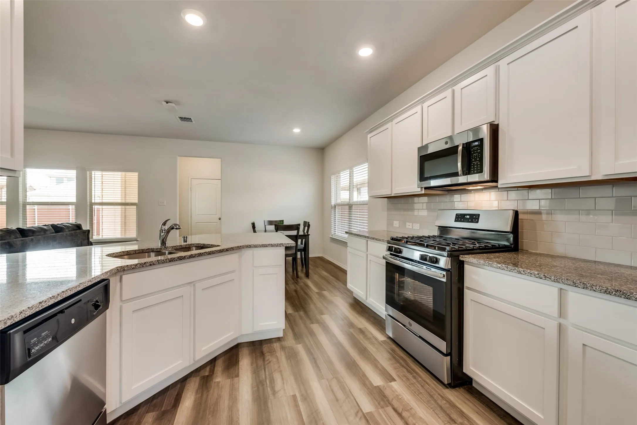 Open-concept kitchen featuring wood-finish flooring, white cabinetry, granite countertops, and stainless steel appliances