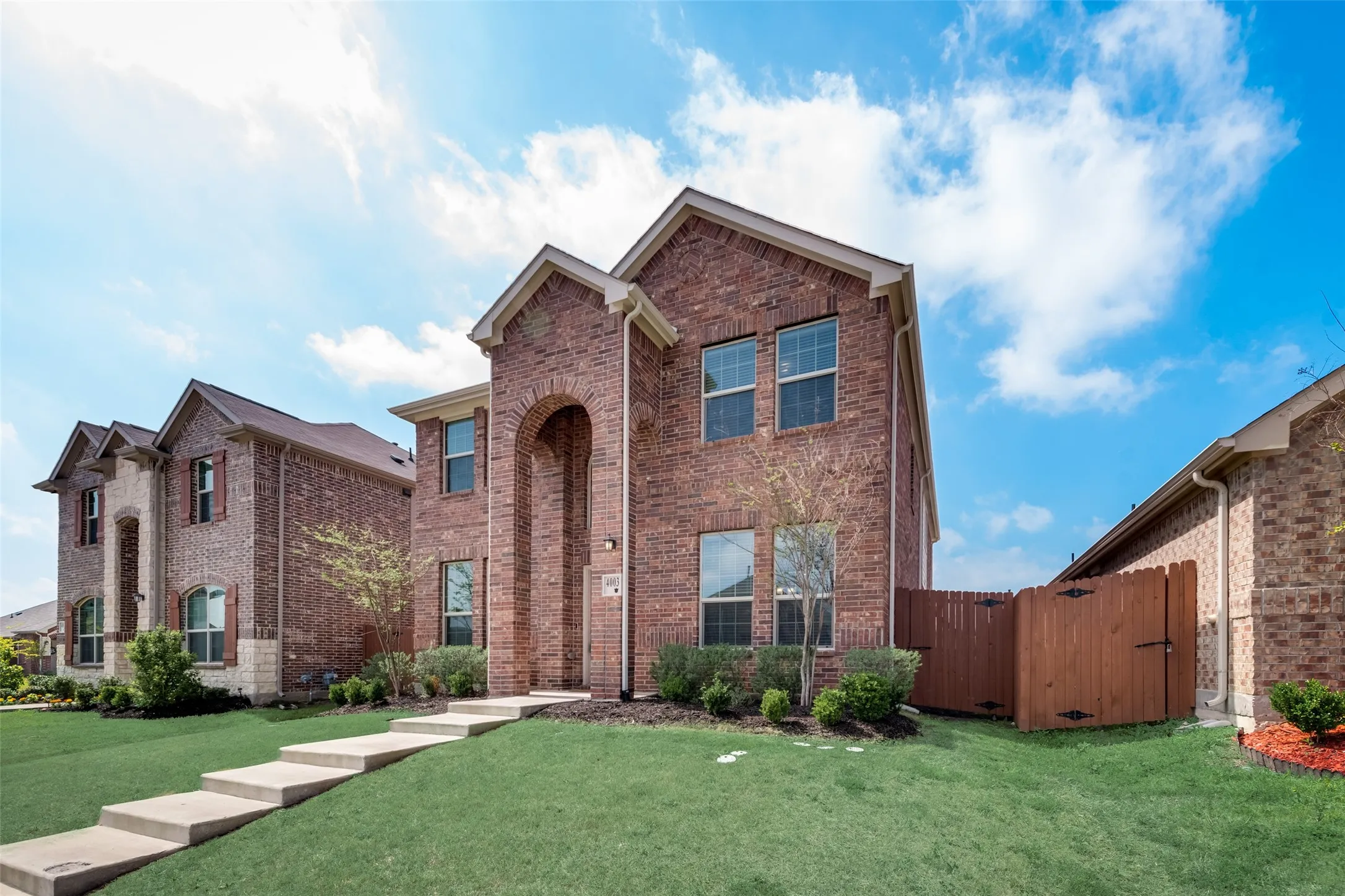 Brick facade residence featuring an arched entryway, multiple windows, a manicured lawn, and a privacy fence