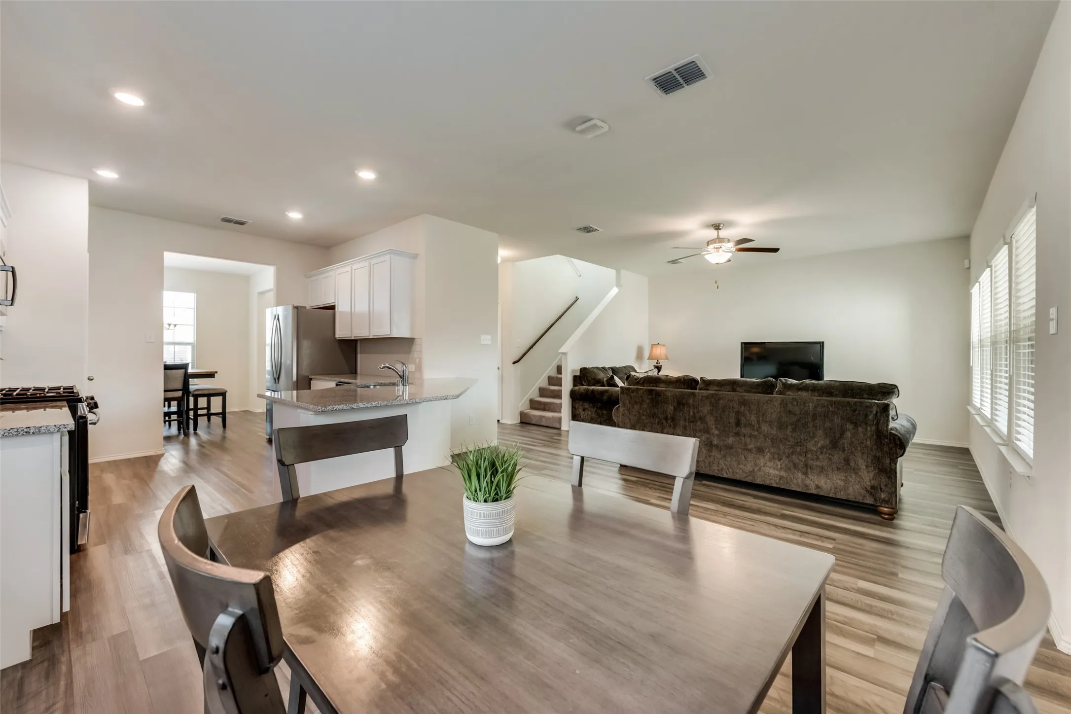 Open-concept interior featuring wood-finish flooring, recessed lighting, and a modern kitchen with white cabinetry and stainless steel appliances