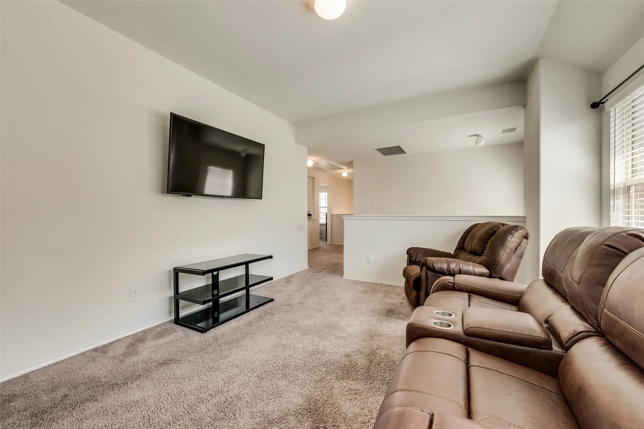 Carpeted living area featuring a wall-mounted television, a media console, a partial wall with a railing, and a window with blinds
