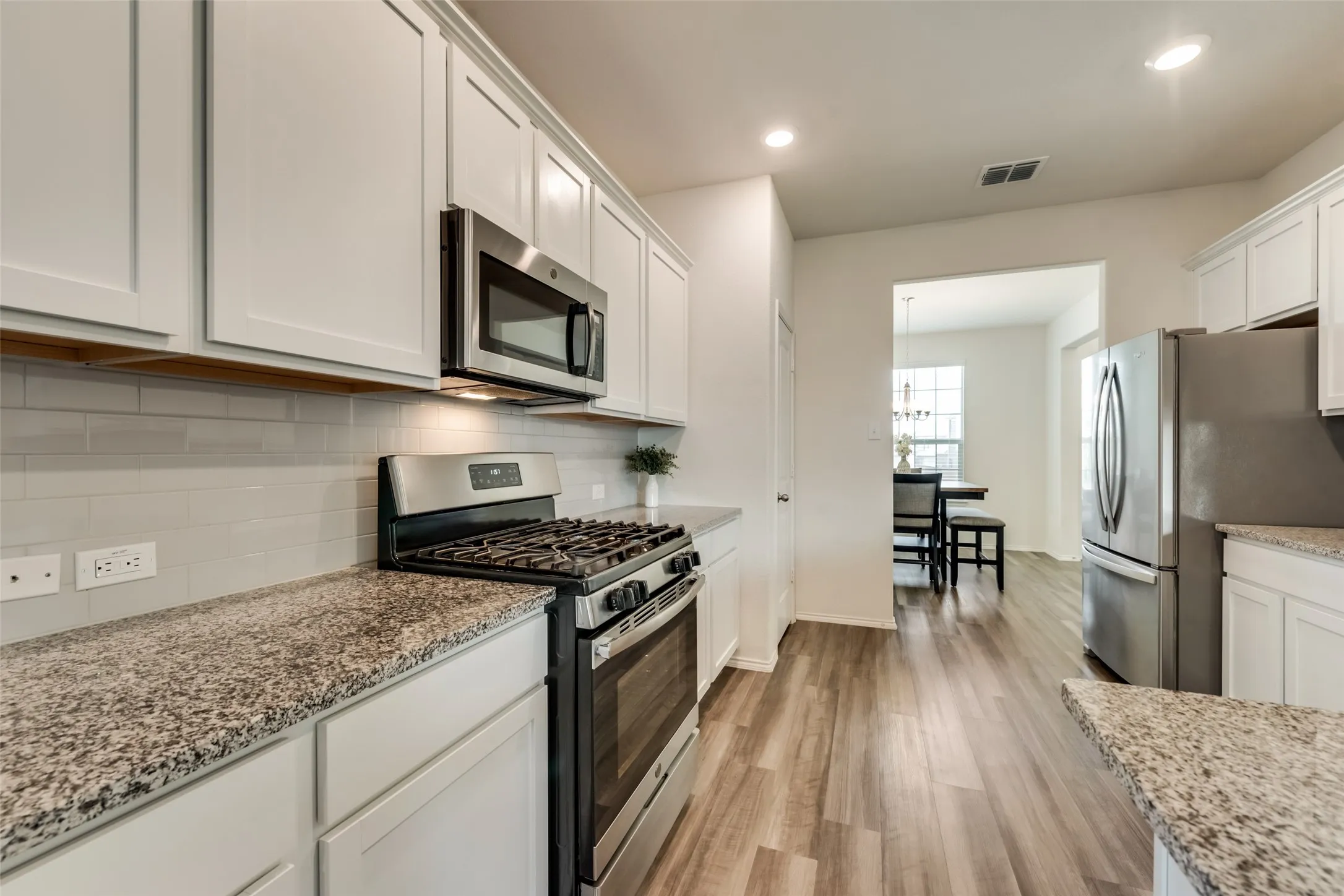 Kitchen featuring white shaker cabinetry, stainless steel appliances, speckled stone countertops, and a subway tile backsplash