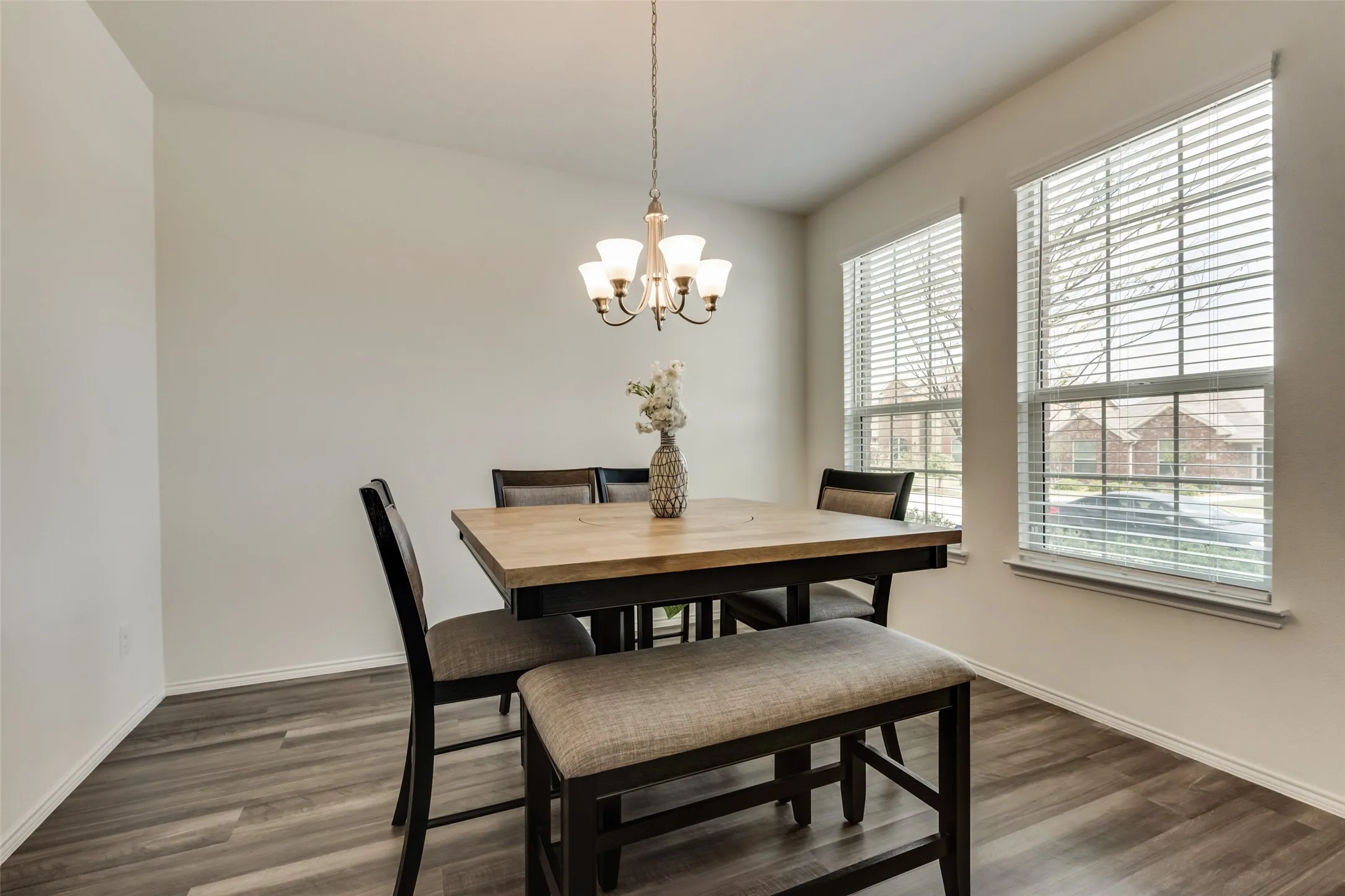 Dining area featuring wood-finish flooring, two large windows with blinds, a ceiling-mounted chandelier, and neutral wall tones