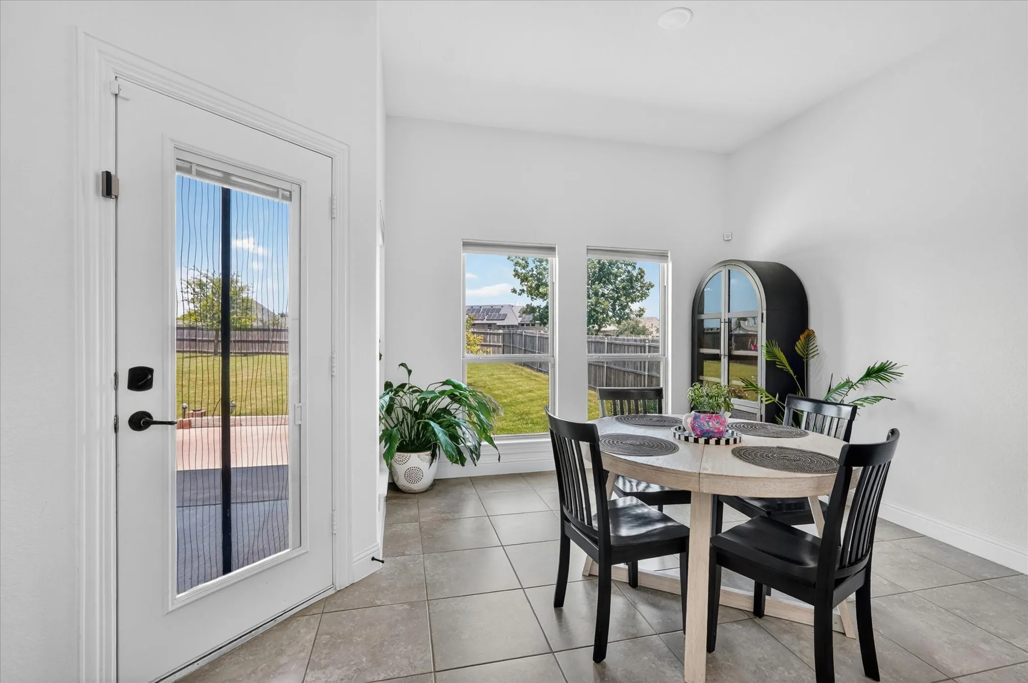 Bright dining area featuring tile flooring, a glass-paned door, and multiple windows overlooking the backyard