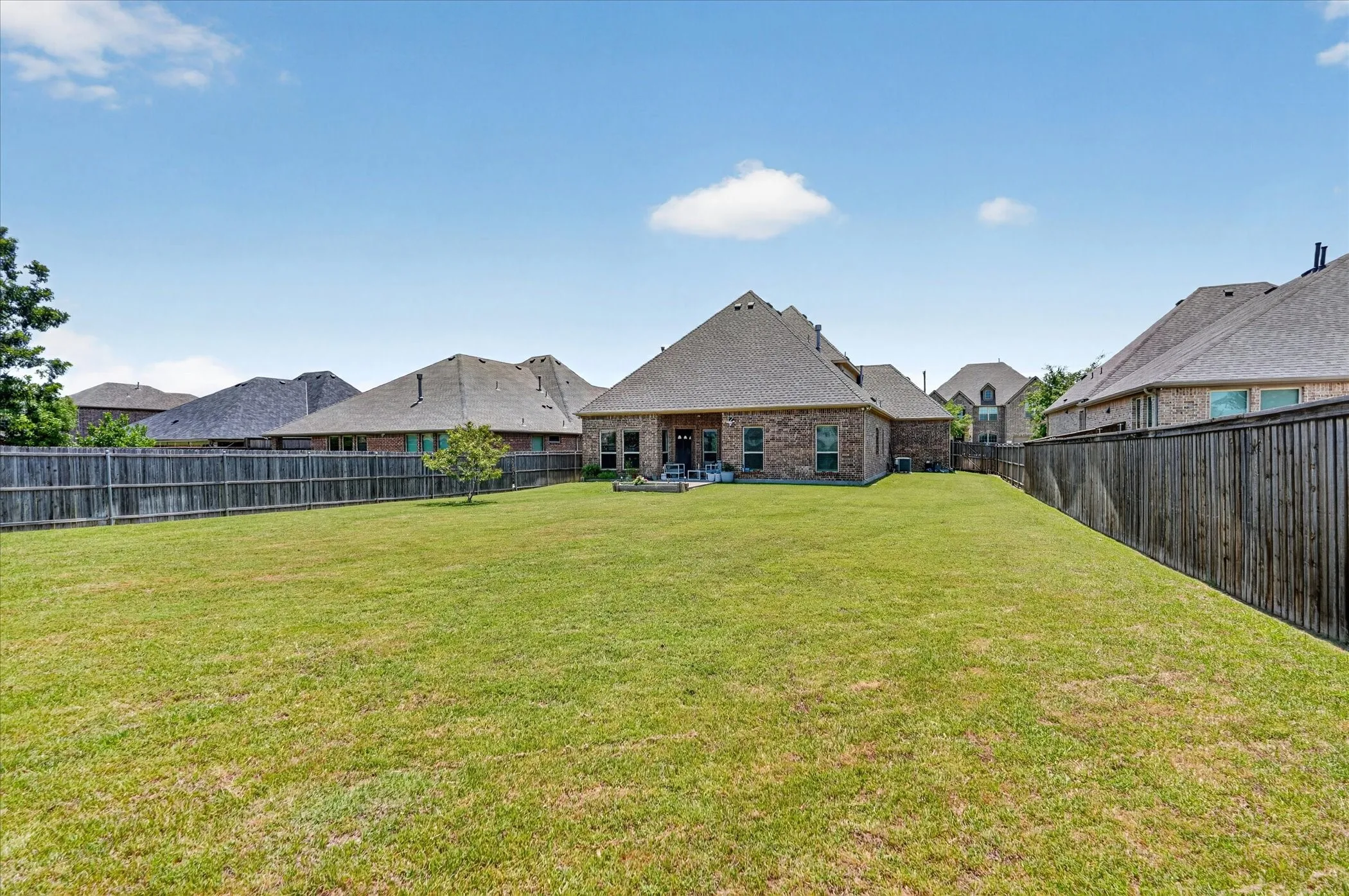 Expansive backyard featuring a manicured lawn, full privacy fencing, and a mature ornamental tree