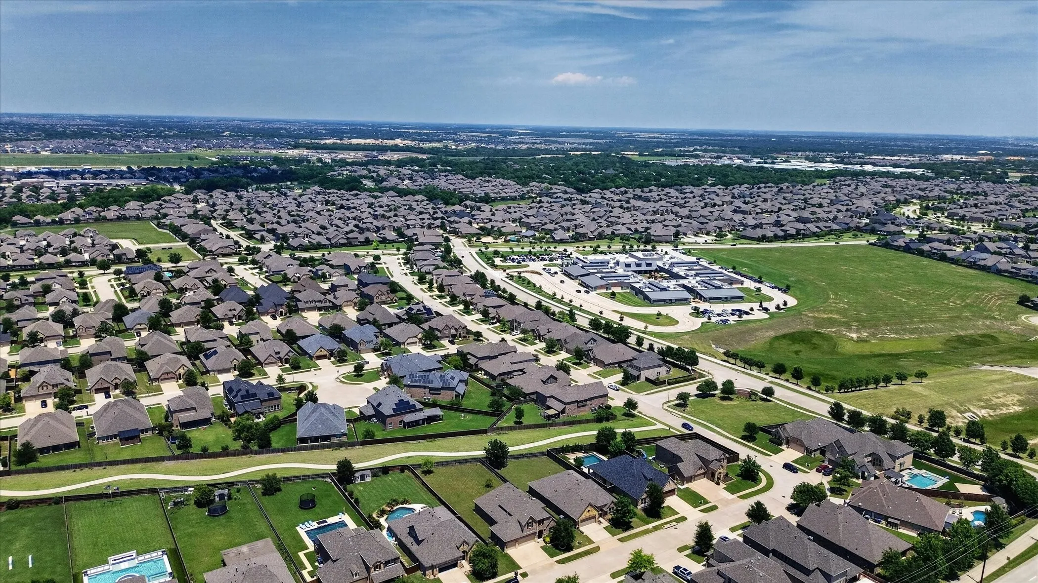 Expansive residential community featuring numerous single-family homes with diverse architectural styles, visible private swimming pools, and a central community building