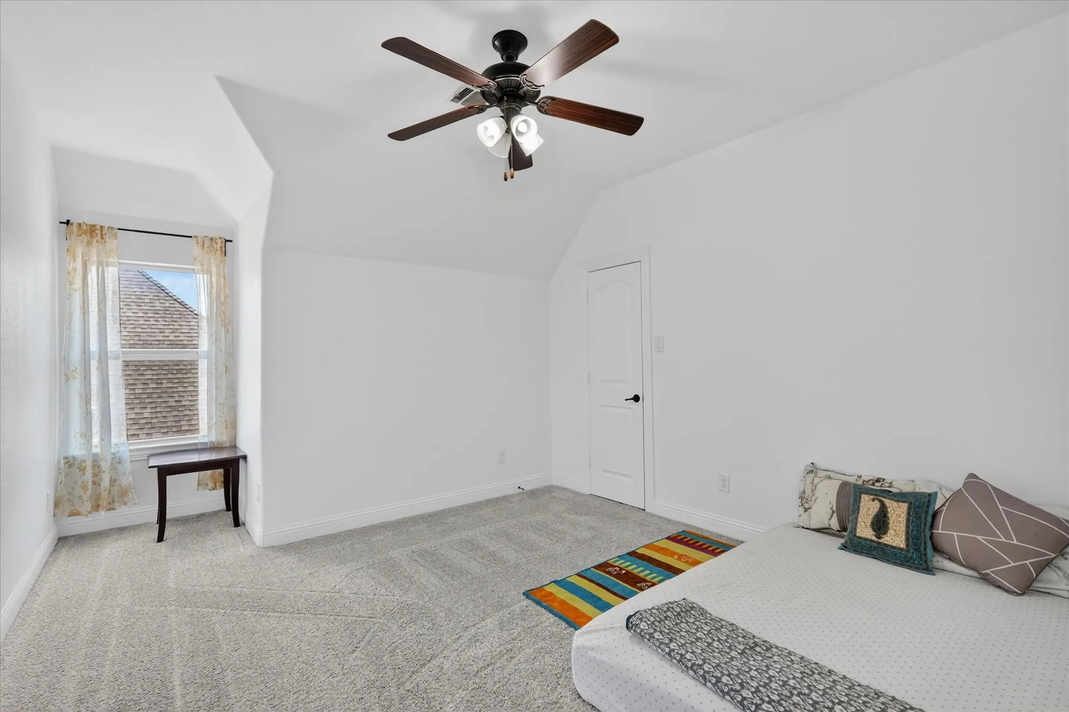 Bright room featuring sloped ceilings, light gray carpet, and a window with sheer curtains