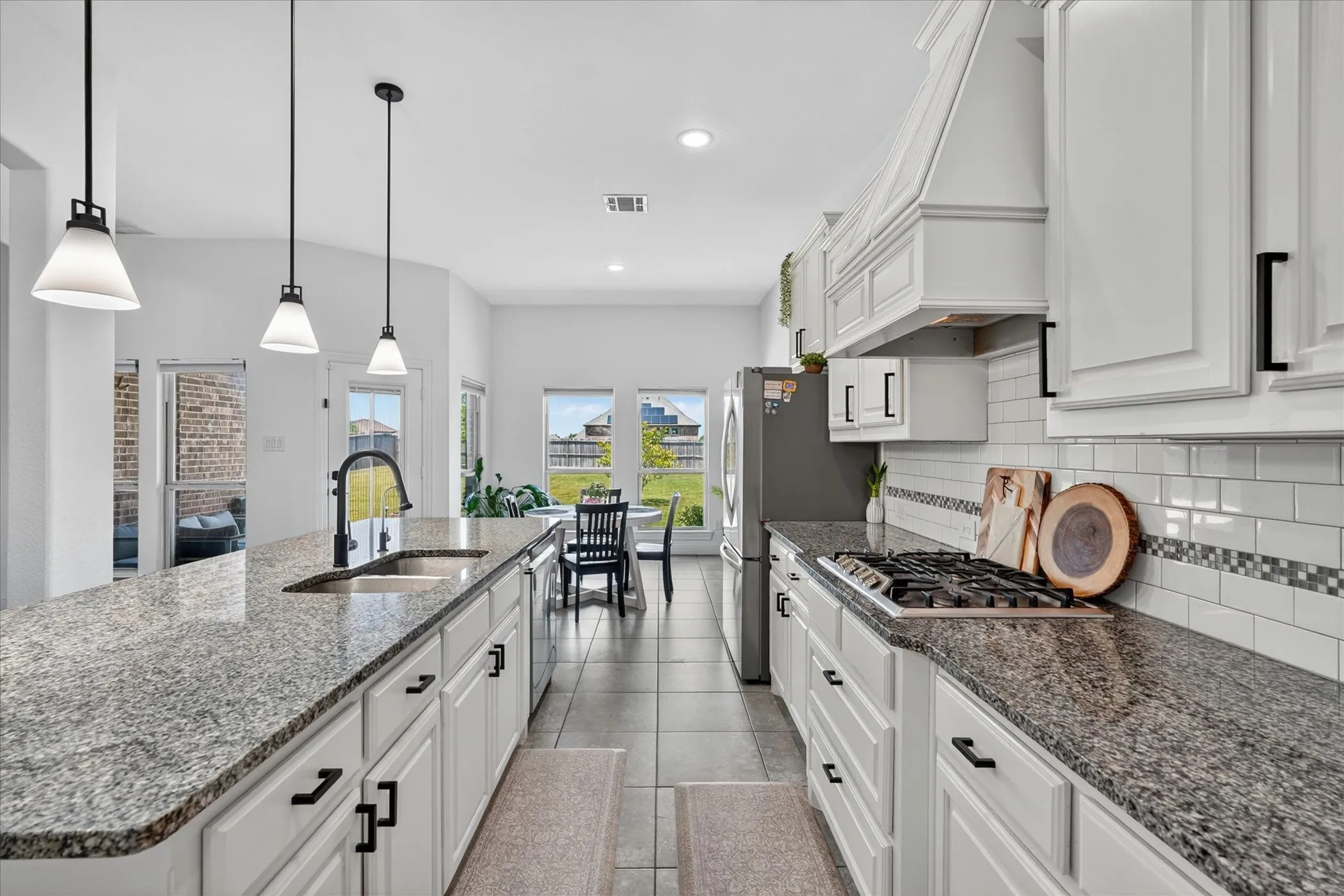 Bright kitchen featuring white cabinetry with black hardware, stone-finish countertops, stainless steel appliances, and tile flooring