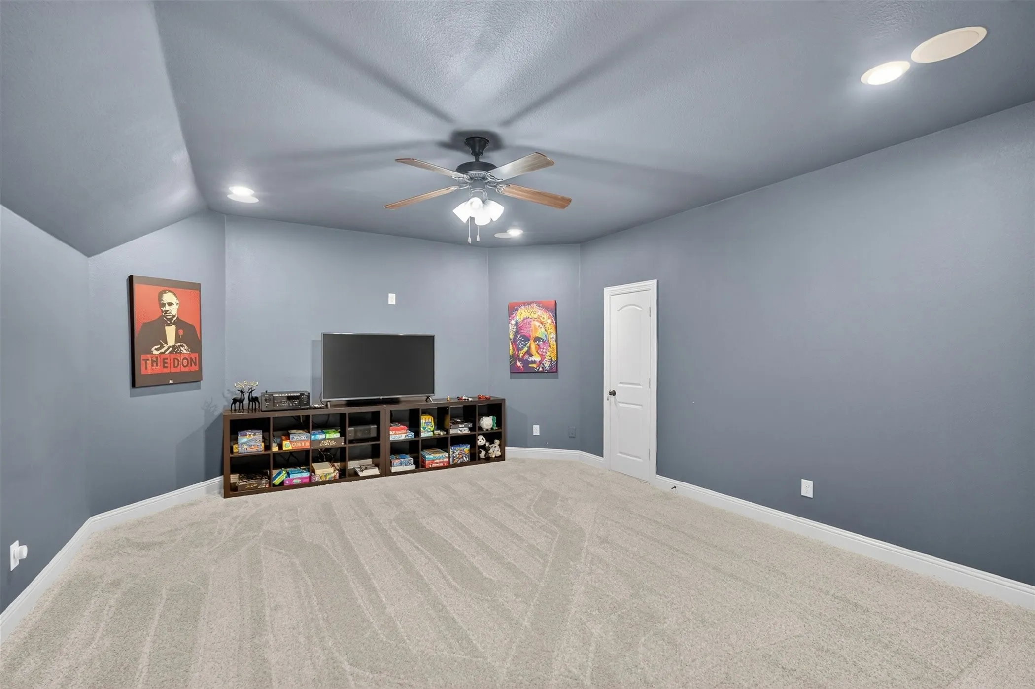 Spacious room featuring sloped ceilings, recessed lighting, ceiling fan, plush carpeting, and a white interior door