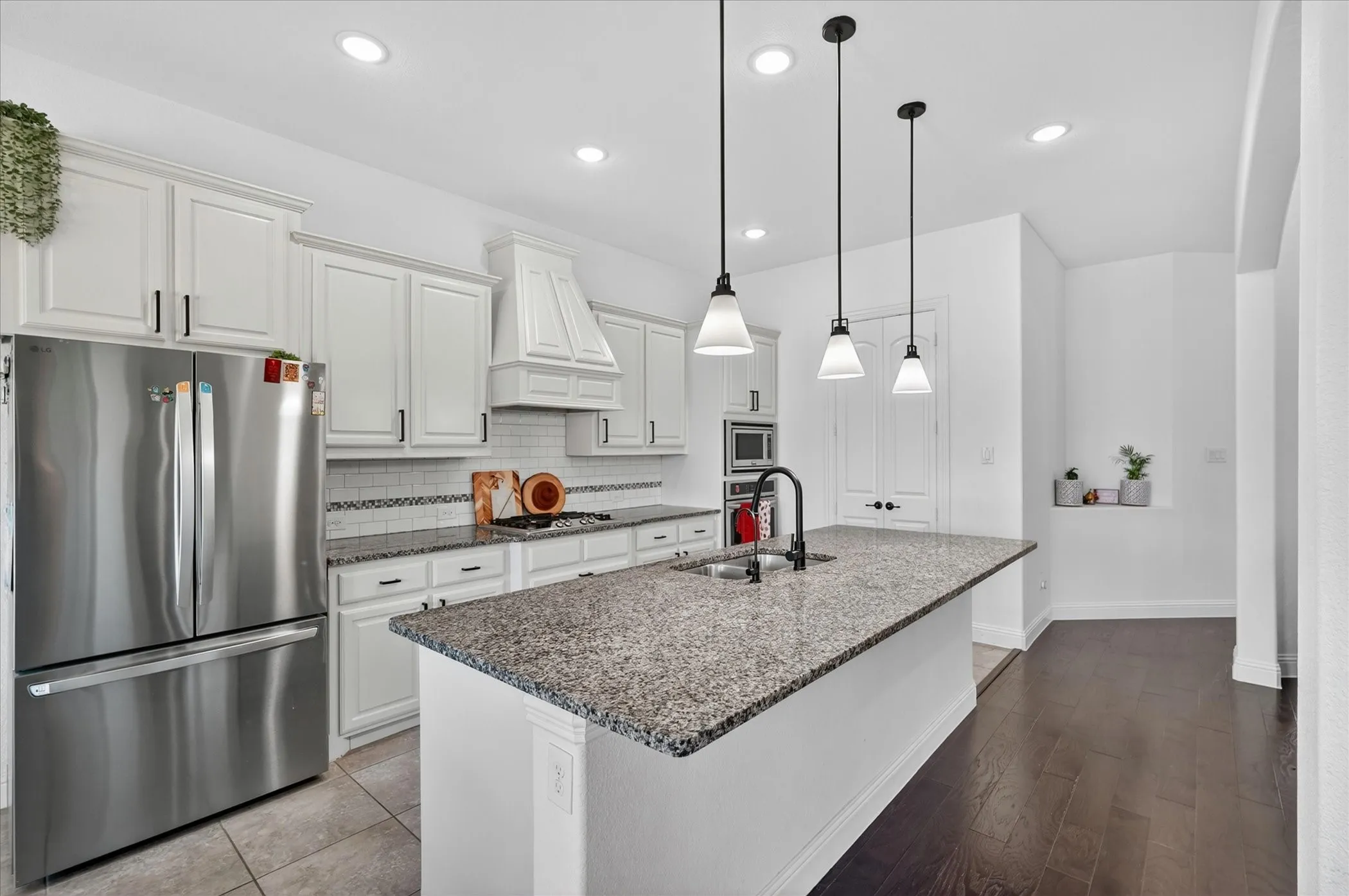 Kitchen featuring a large island with a stone countertop, stainless steel appliances, white cabinetry with dark hardware, a white tile backsplash, and recessed lighting