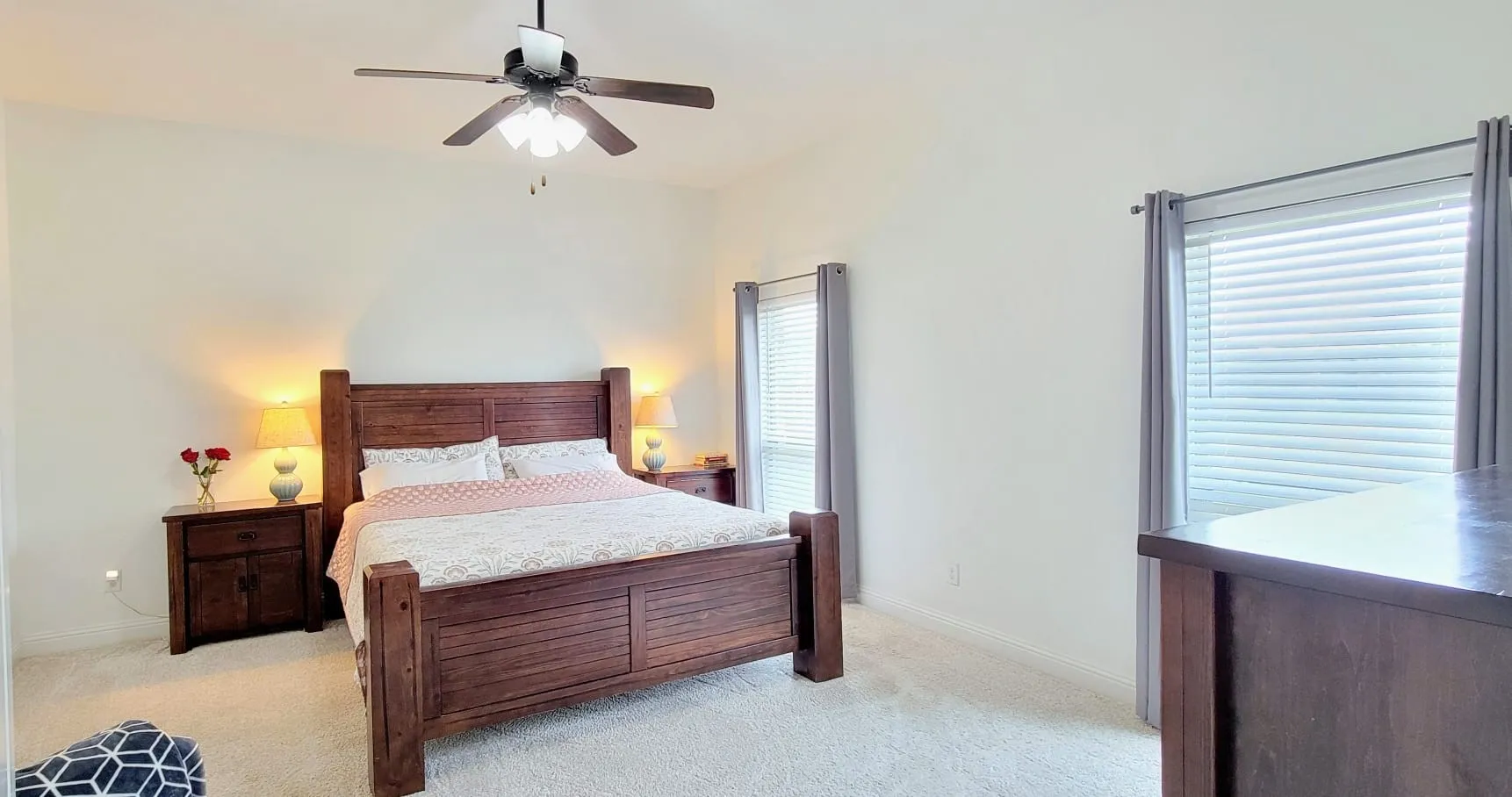 Spacious room featuring vaulted ceilings, light-colored carpeting, two windows with blinds and drapes, and a ceiling fan with integrated lighting