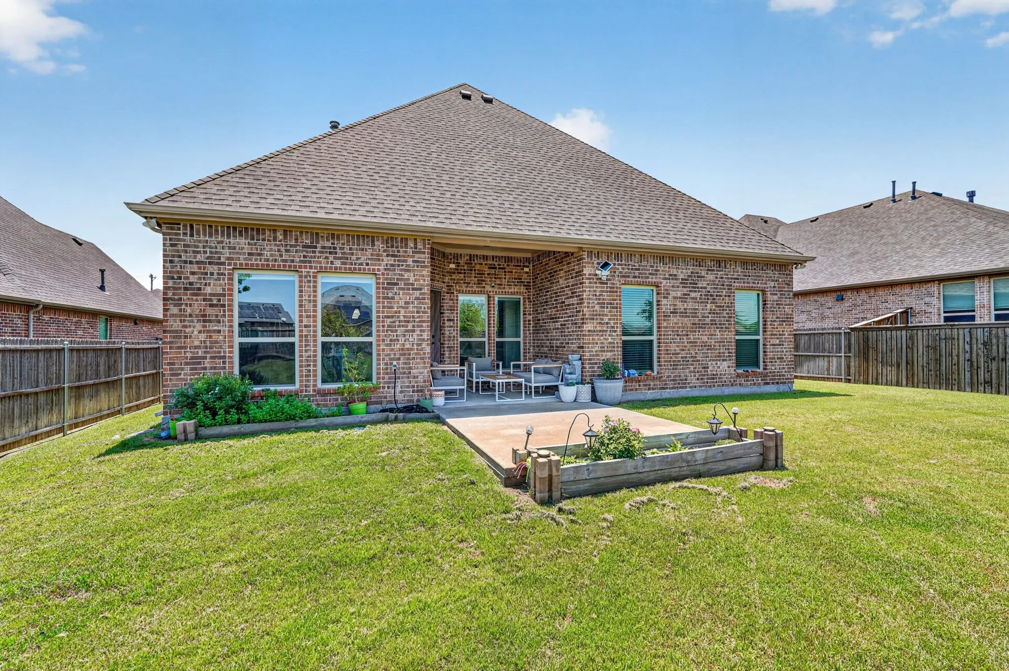Brick exterior featuring a spacious rear lawn, concrete patio, and an elevated garden bed