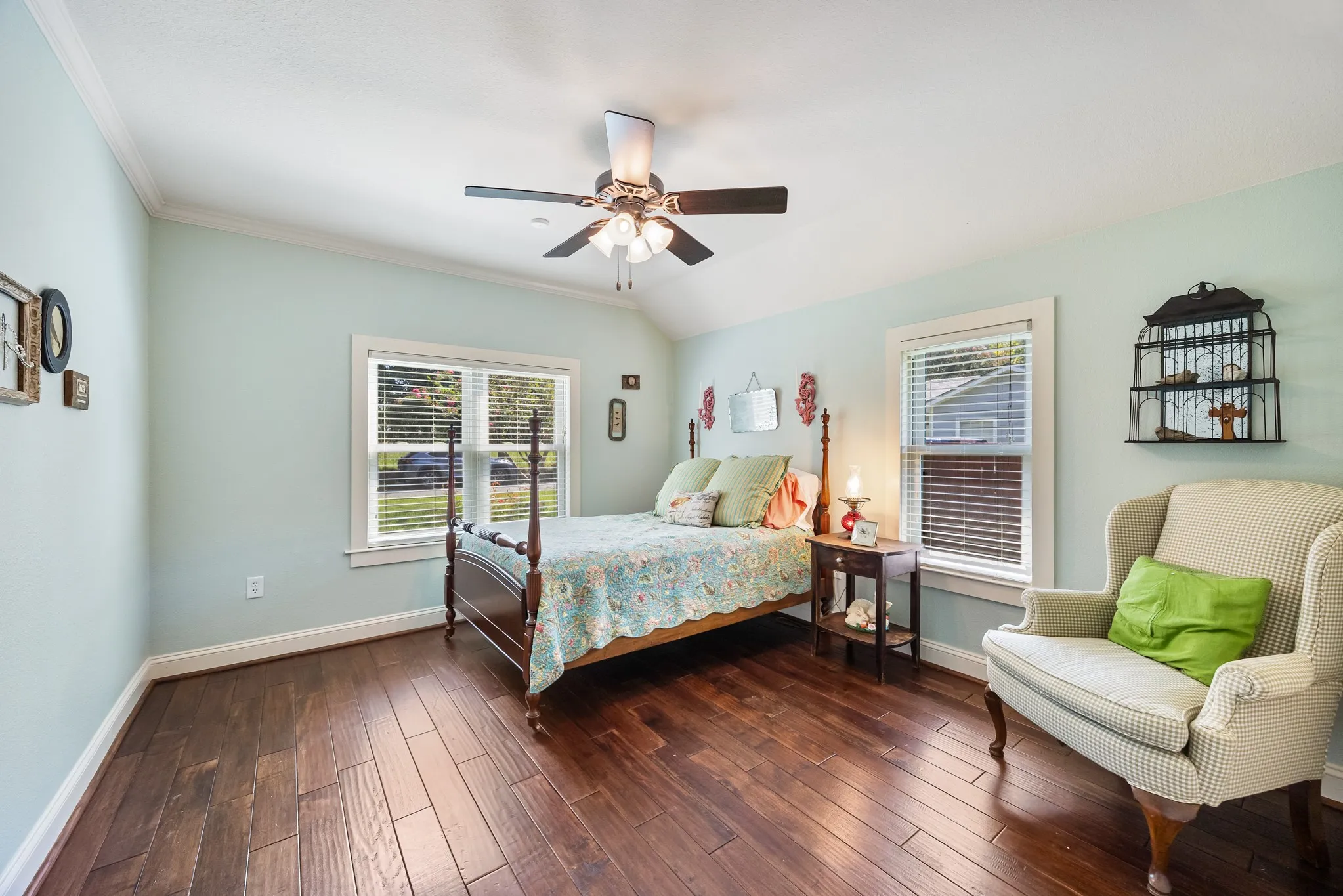 Vaulted ceiling with an installed ceiling fan, two windows with blinds, wood-finish flooring, and white baseboards