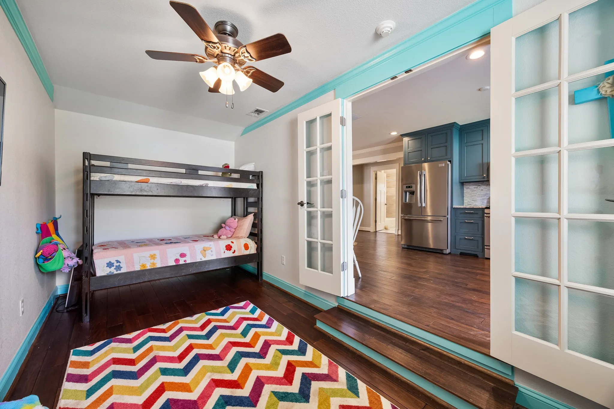 Room featuring wood-finish flooring, a ceiling fan with integrated lighting, and white walls with a teal trim