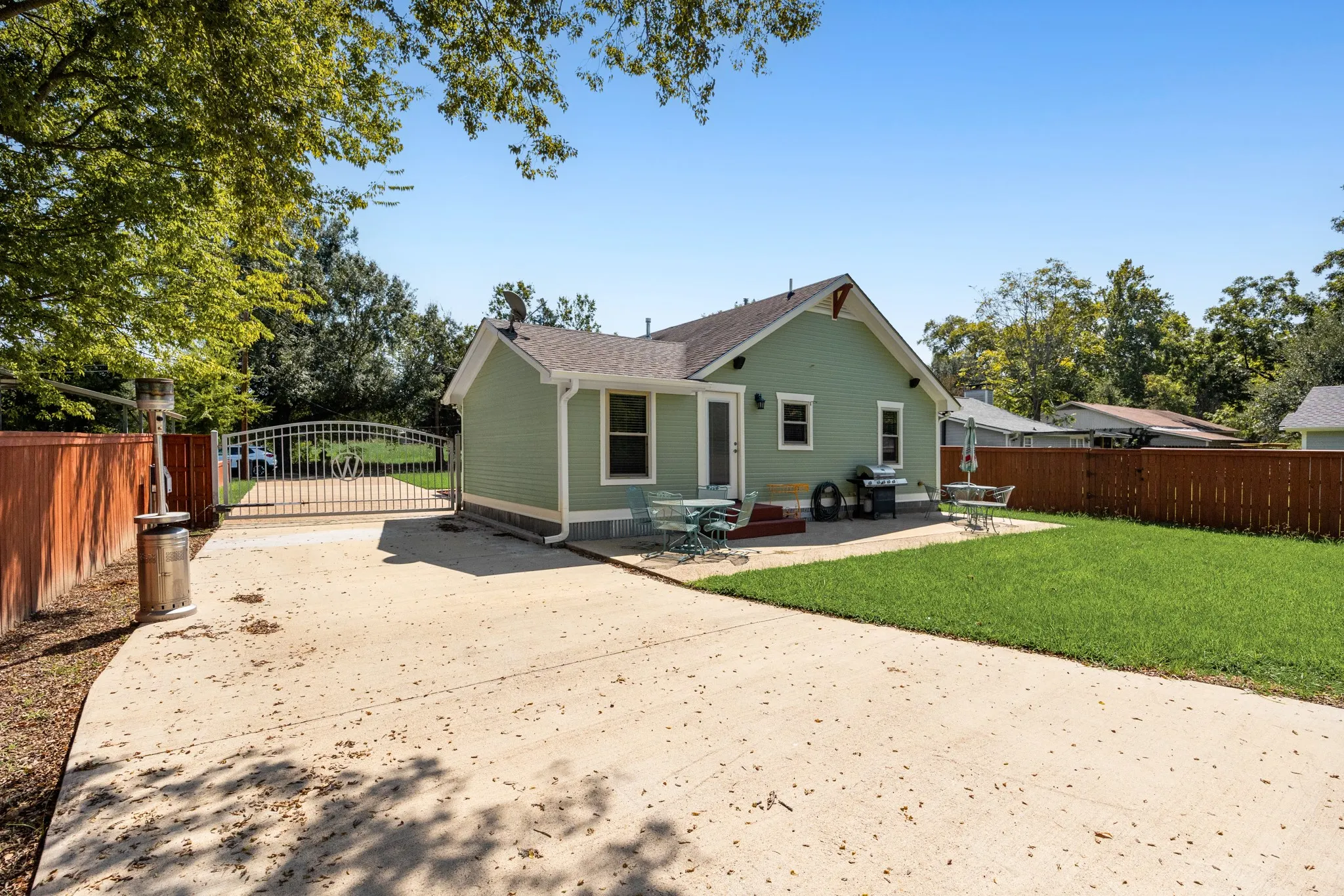 Green siding residence with a concrete patio, expansive concrete driveway, fenced yard, manicured lawn, and arched metal gate