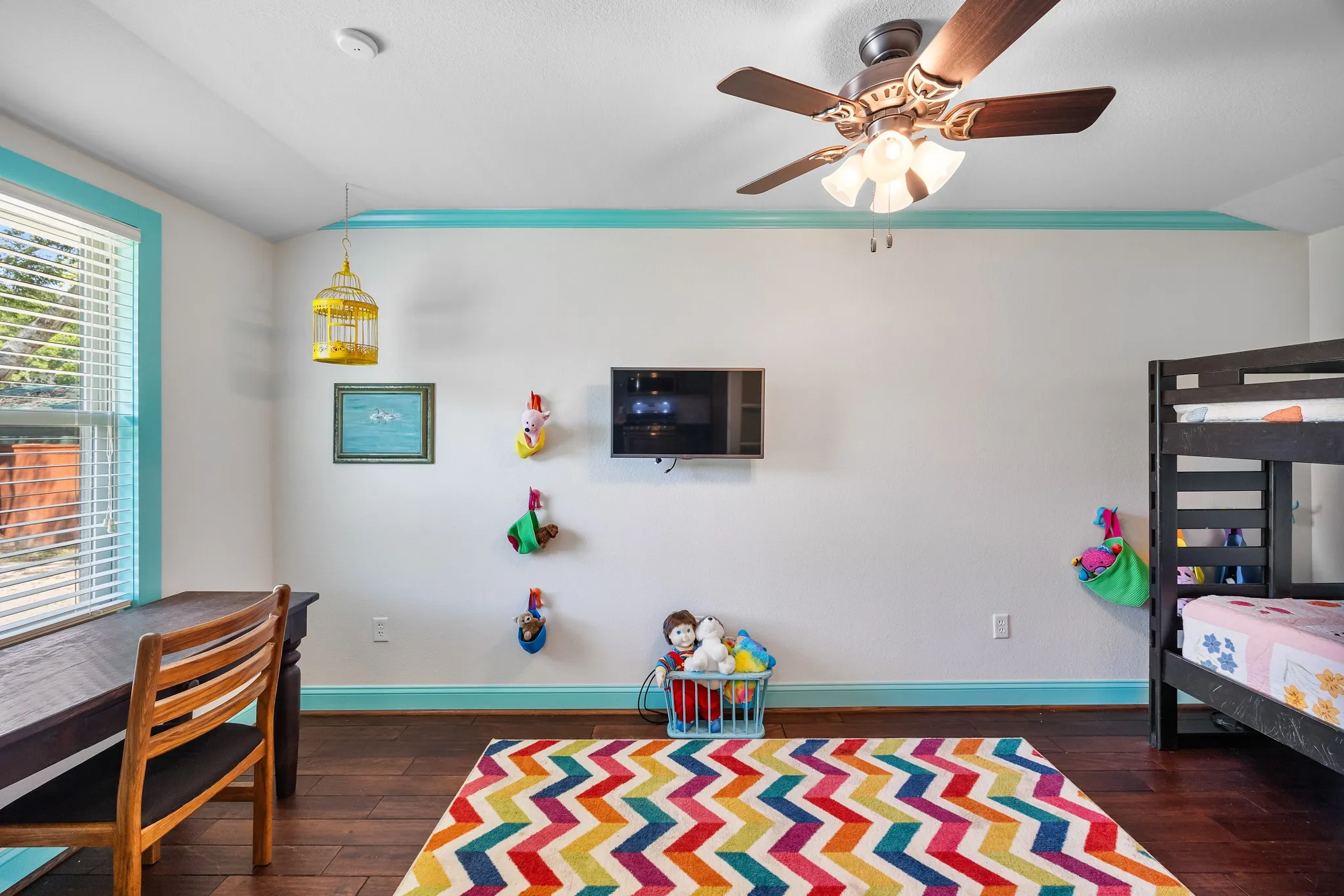 Interior room featuring rich wood-finish flooring, white walls with turquoise trim, a ceiling fan with integrated lighting, and a window with horizontal blinds