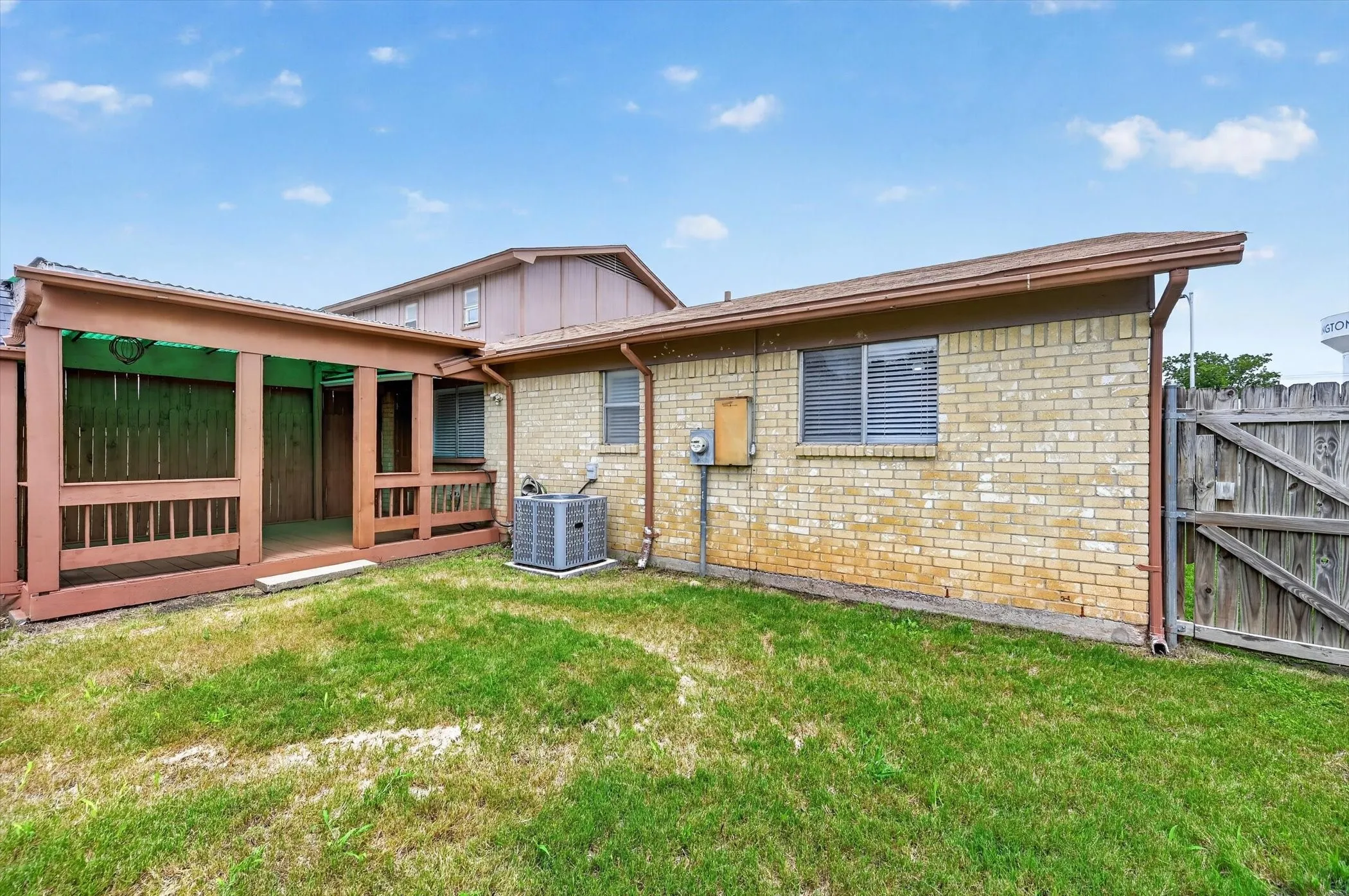 Expansive grassy area featuring a covered porch with wood railing, a brick exterior, and a wooden privacy fence