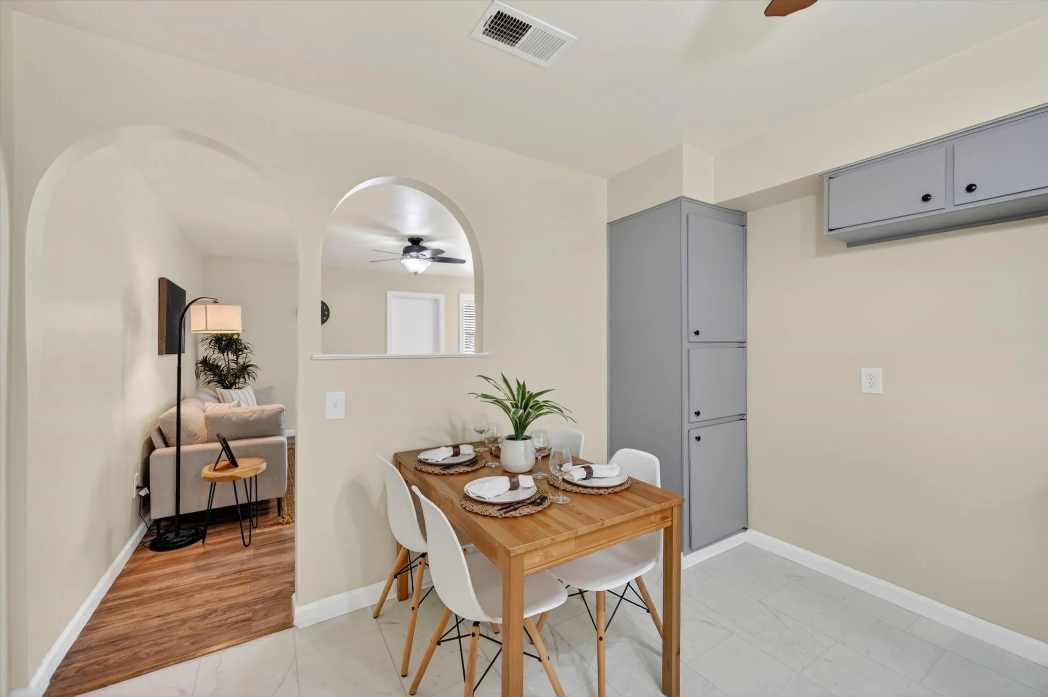 Dining area with light tile flooring, built-in gray cabinetry, and an arched pass-through to a room with wood-finish flooring