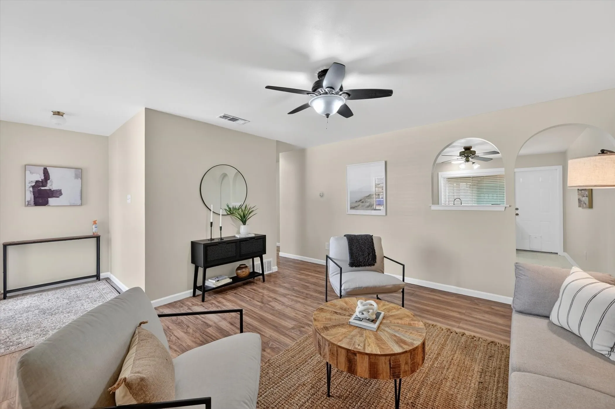 Spacious living area featuring wood-finish flooring, a ceiling fan with integrated lighting, and neutral wall tones