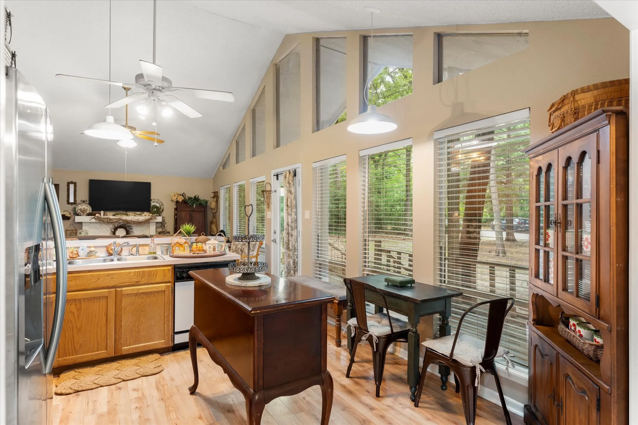 Kitchen area featuring vaulted ceilings, wood-finish flooring, a stainless steel refrigerator, light wood cabinetry, and a sink with a window