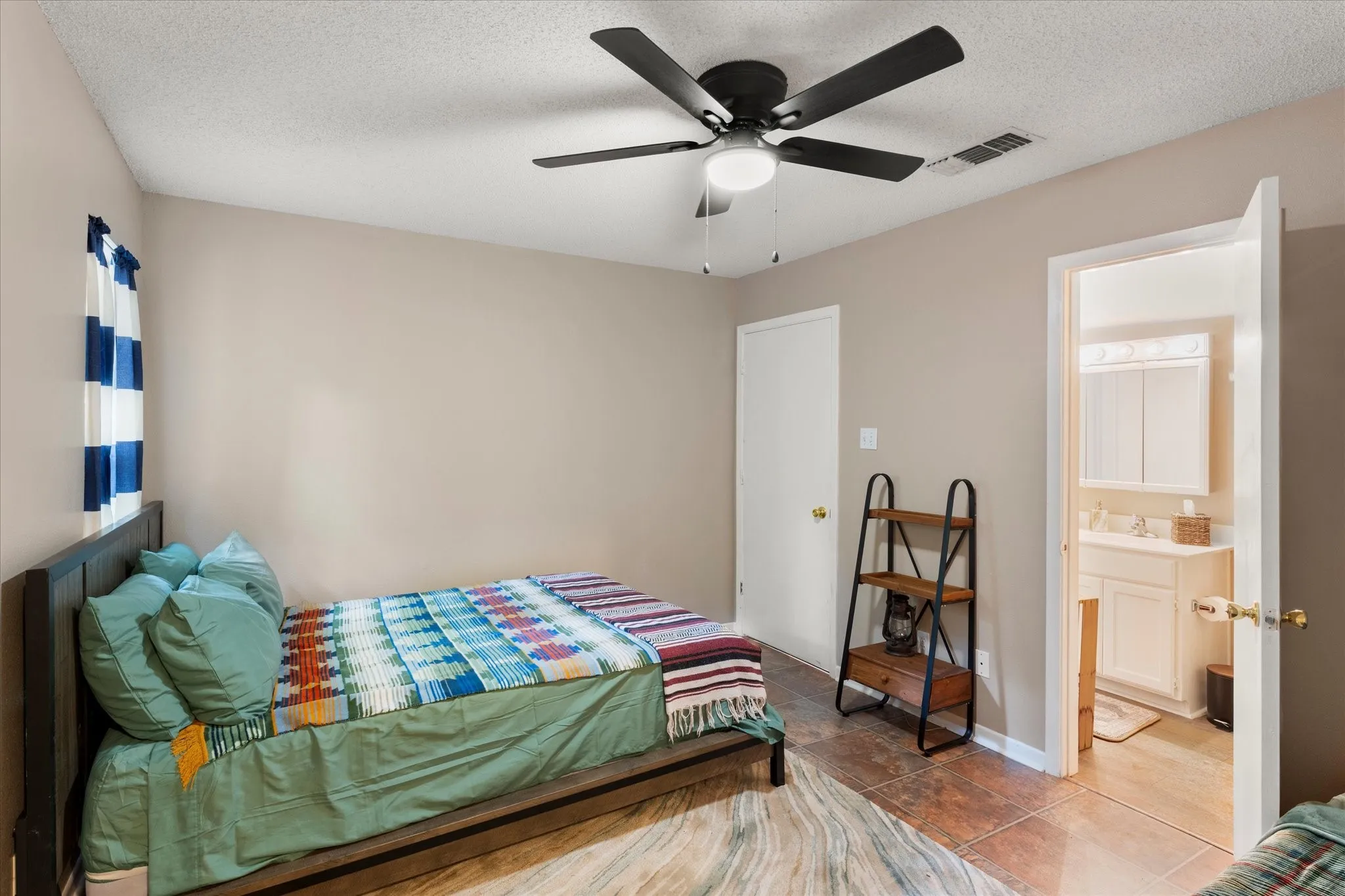 Bedroom featuring a ceiling fan with integrated lighting, wood-finish flooring, and a door leading to a bathroom with a white vanity and medicine cabinet
