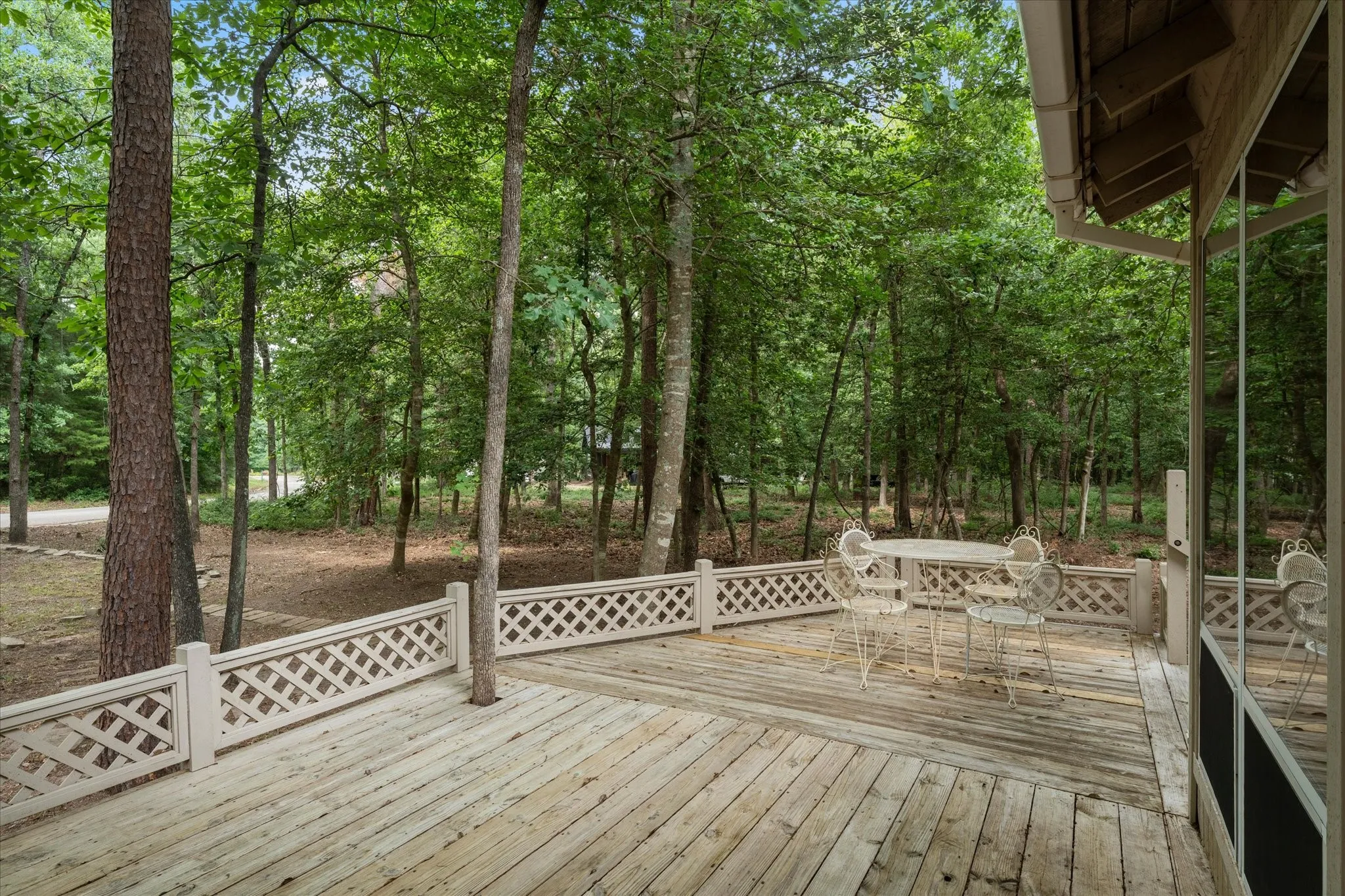 Expansive wood deck with lattice railing, surrounded by mature trees