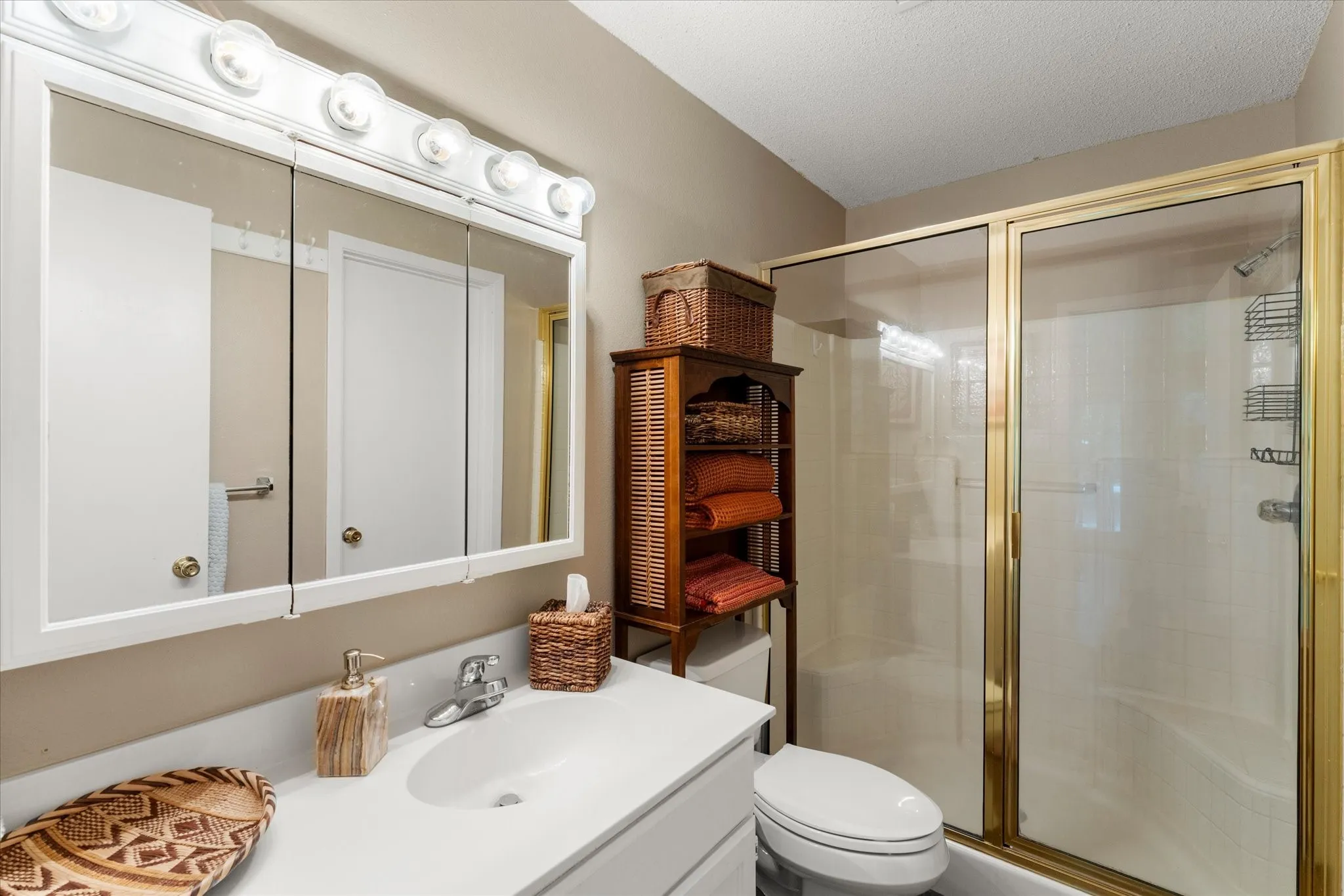 Bathroom featuring a vanity with an integrated sink, a three-door medicine cabinet with overhead lighting, and a shower-tub combination with a gold-finish frame