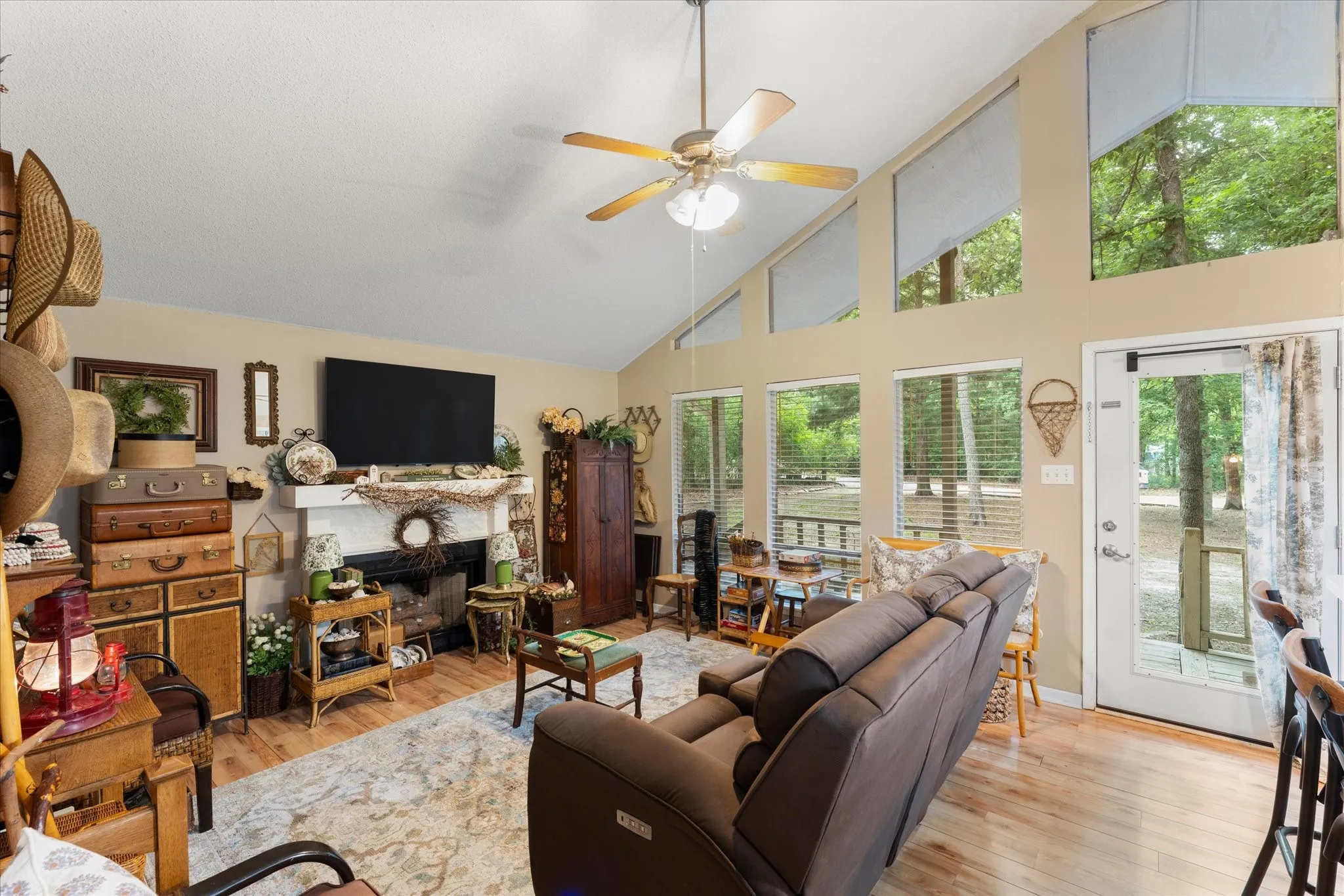 Vaulted ceiling living area featuring wood-finish flooring, a fireplace with a white mantel, and extensive windowing with transom elements