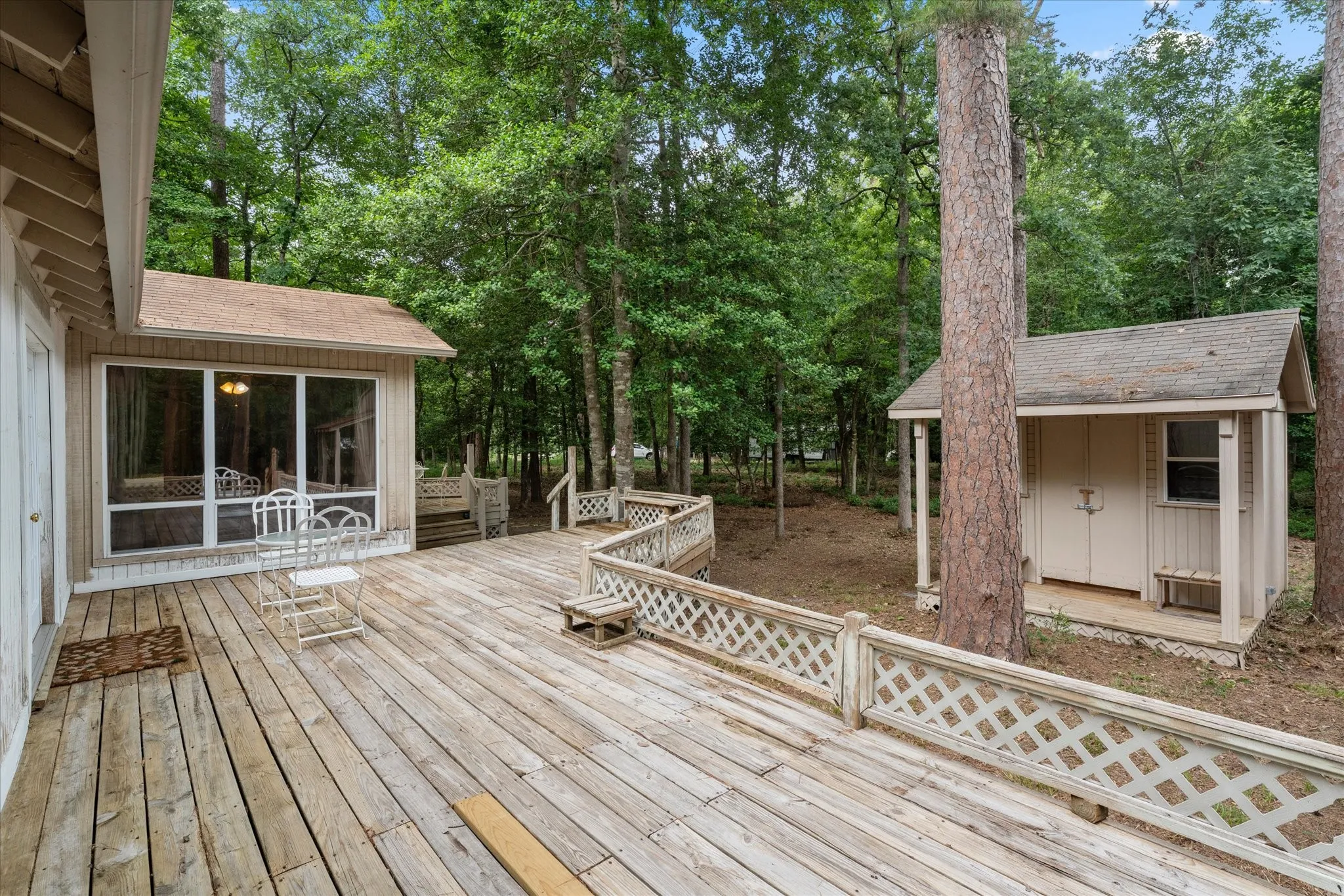 Expansive wood deck with lattice railing, featuring a screened-in porch with a shingled roof and a detached storage shed with a shingled roof