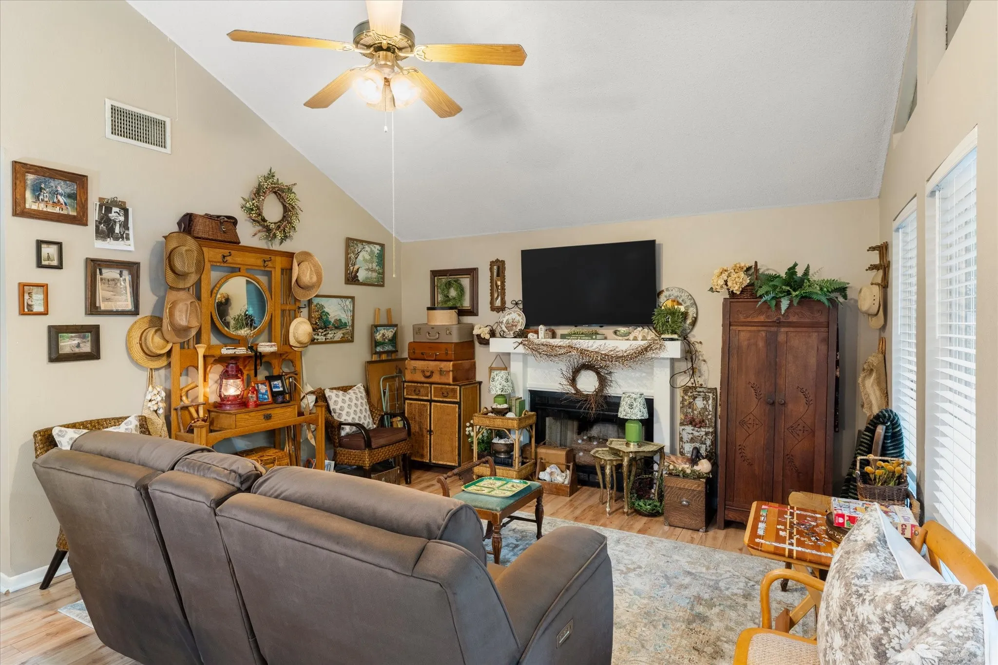 Living area featuring vaulted ceilings, a ceiling fan with integrated lighting, wood-finish flooring, and multiple windows with blinds