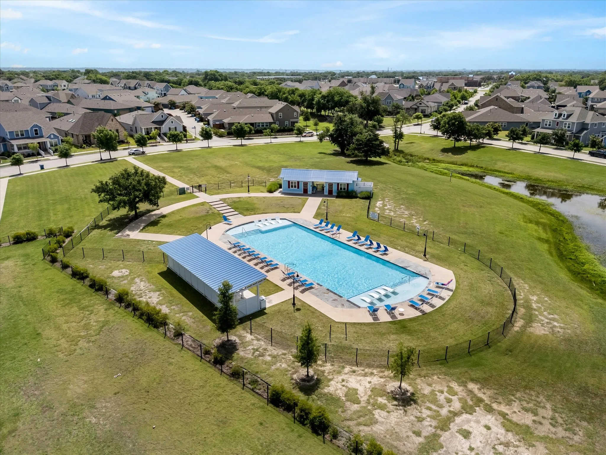 Community swimming pool with surrounding lounge chairs, covered shade structure, and a pool house