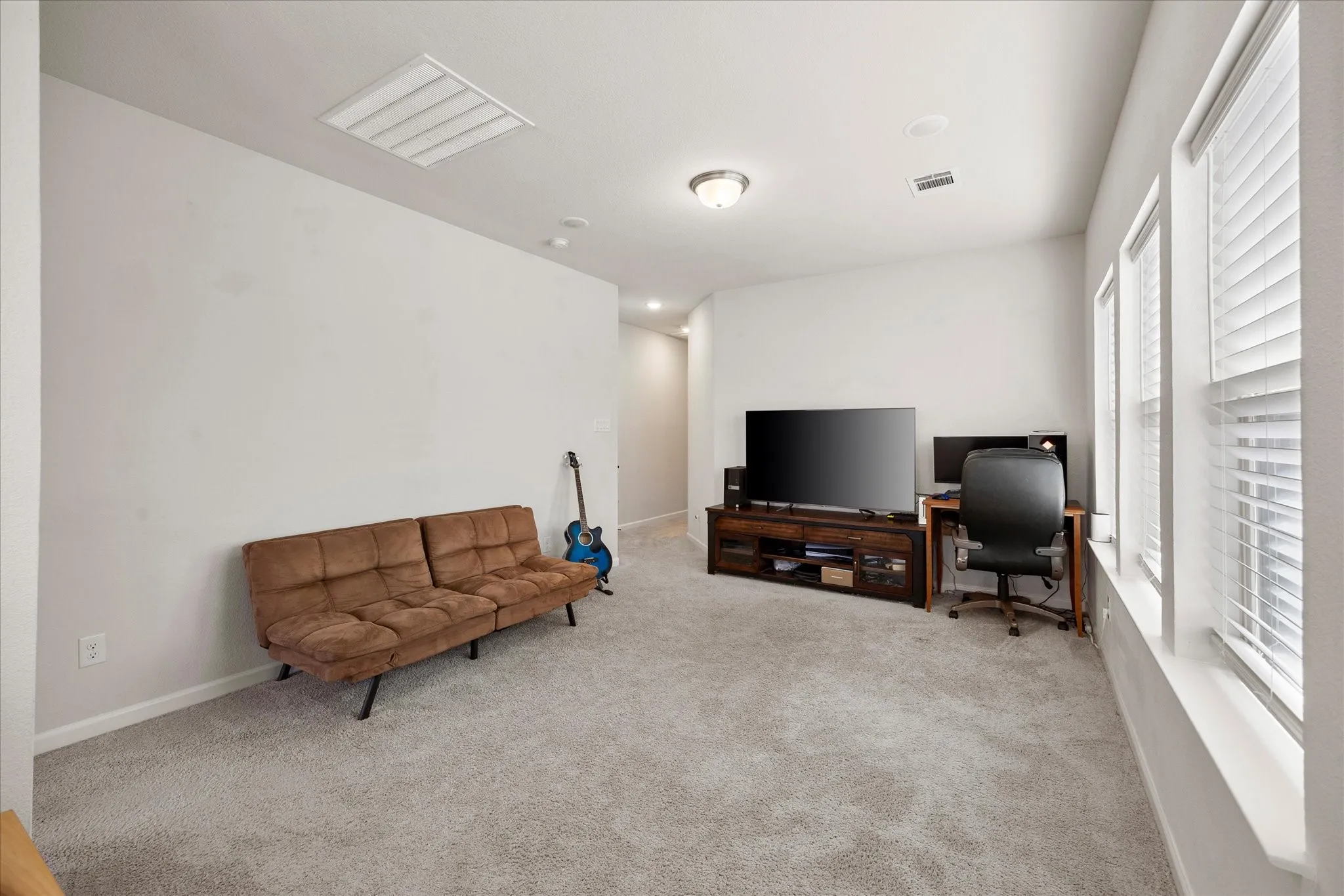 Spacious carpeted room featuring multiple windows with blinds, a ceiling-mounted light fixture, recessed lighting, and white baseboards