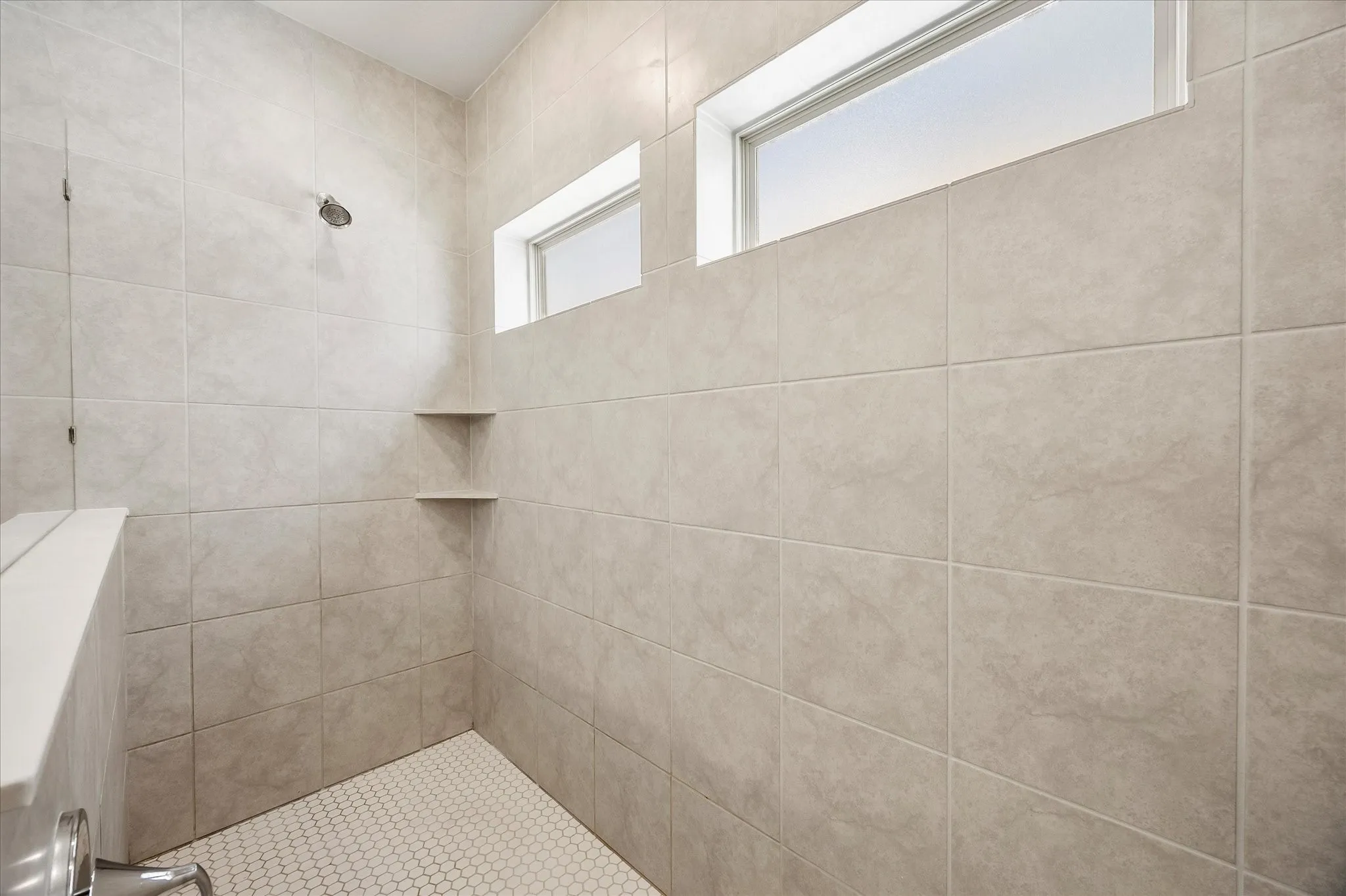 Shower featuring large format wall tiling, a hex tile floor, two corner shelves, a shower head fixture, and two transom windows