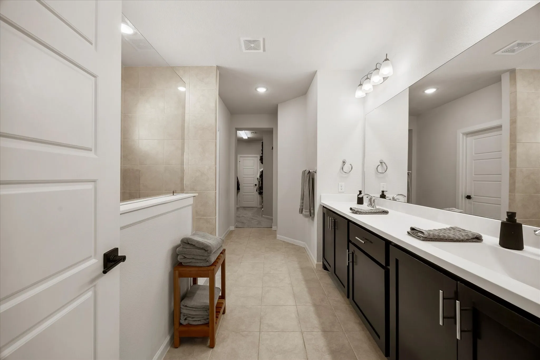Spacious bathroom featuring a dual vanity with dark cabinetry, integrated rectangular sinks, and a large wall-mounted mirror