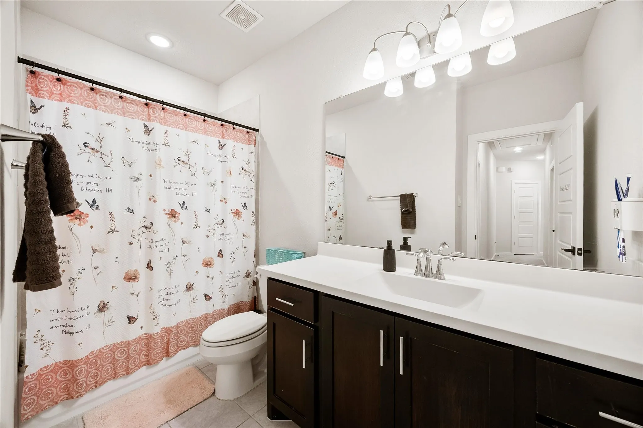 Bathroom featuring a single vanity with a dark wood-finish cabinet and white countertop, an integrated sink, and a wall-mounted mirror