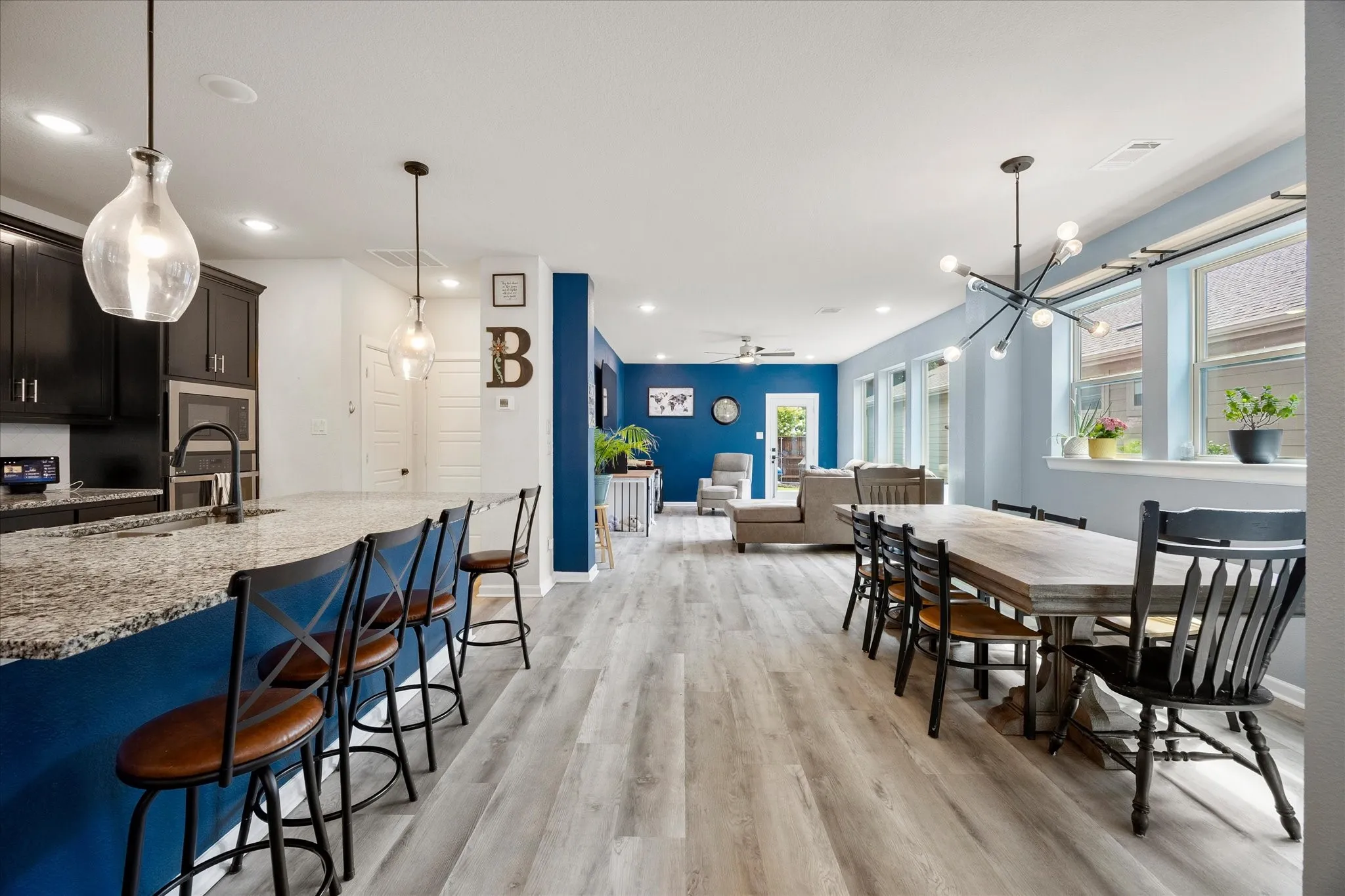 Open-concept living area featuring light wood-finish flooring, a kitchen island with stone countertops, dark cabinetry, and pendant lighting