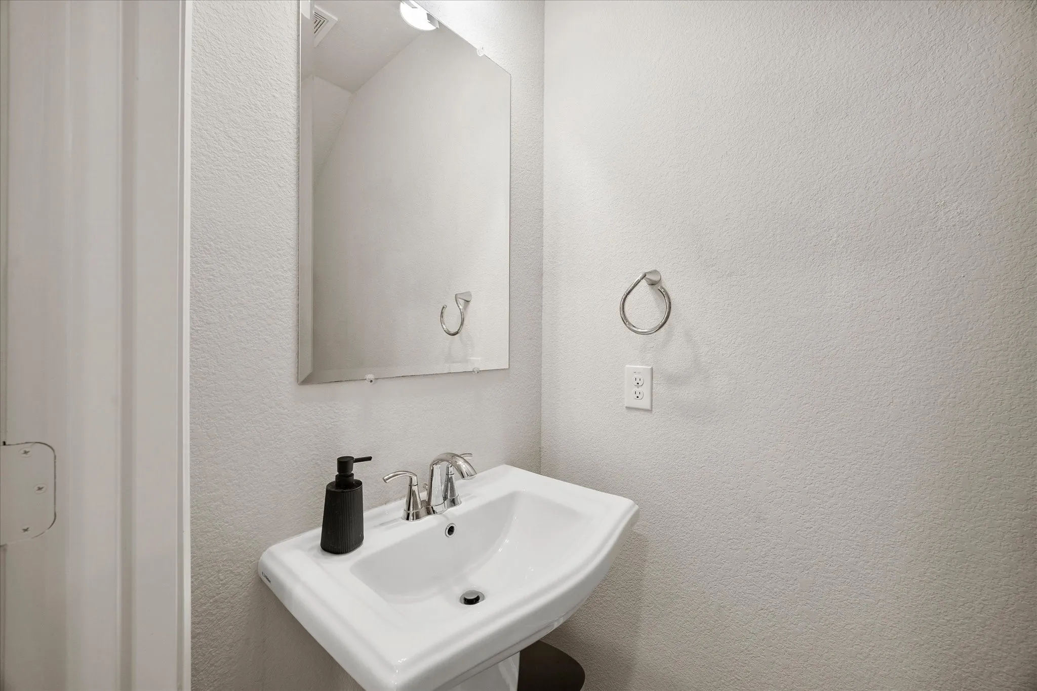 Pedestal sink with chrome faucet, framed mirror, and textured wall finish