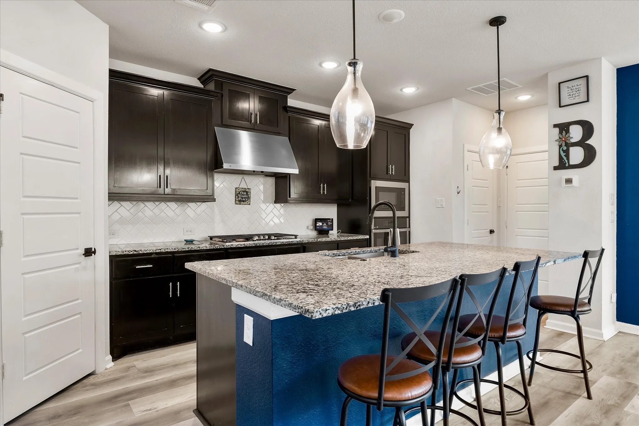 Kitchen featuring a spacious island with a granite-style countertop, dark cabinetry, and wood-finish flooring