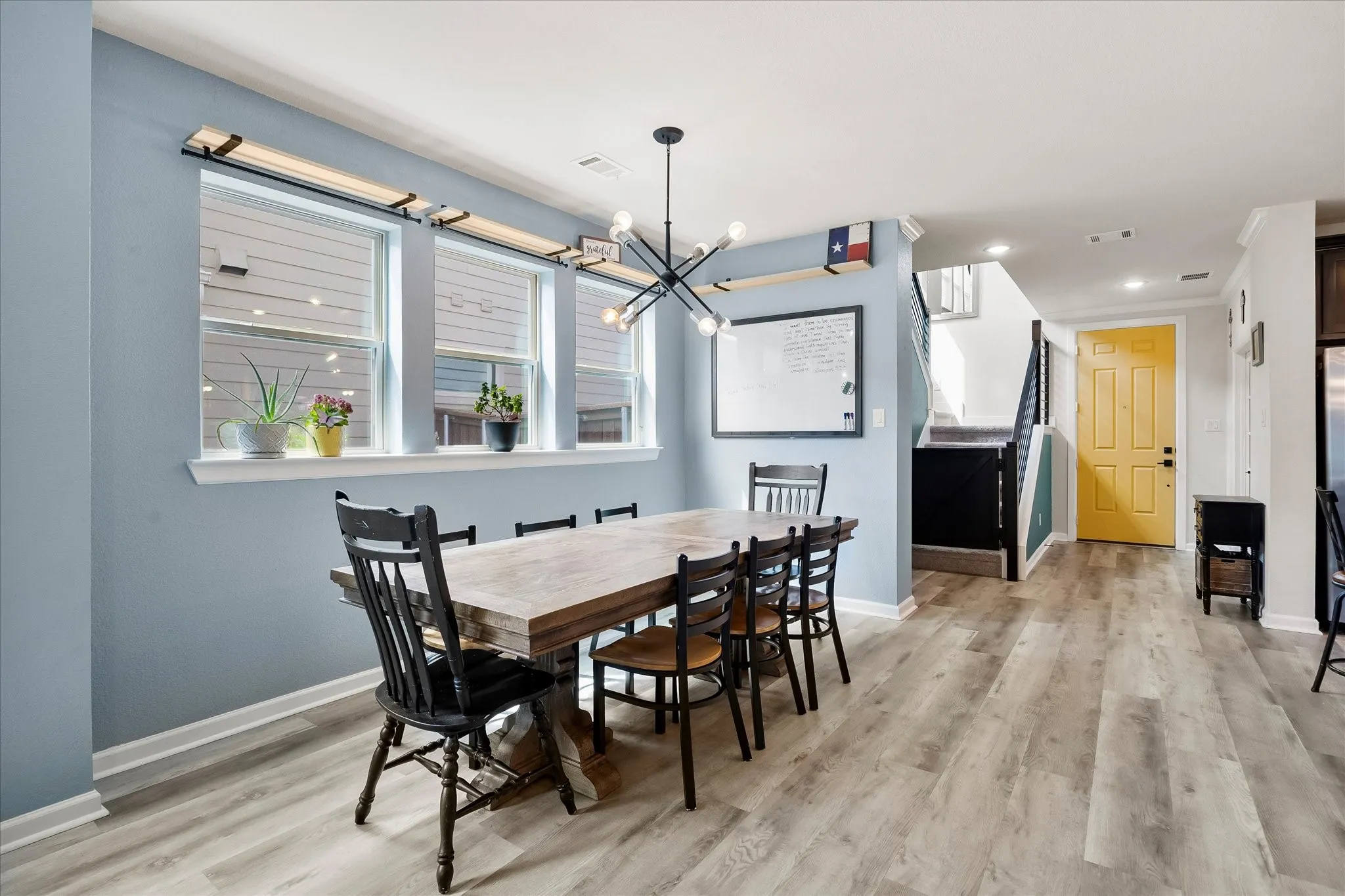 Dining area featuring wood-finish flooring, a modern chandelier, and a trio of windows with white sills