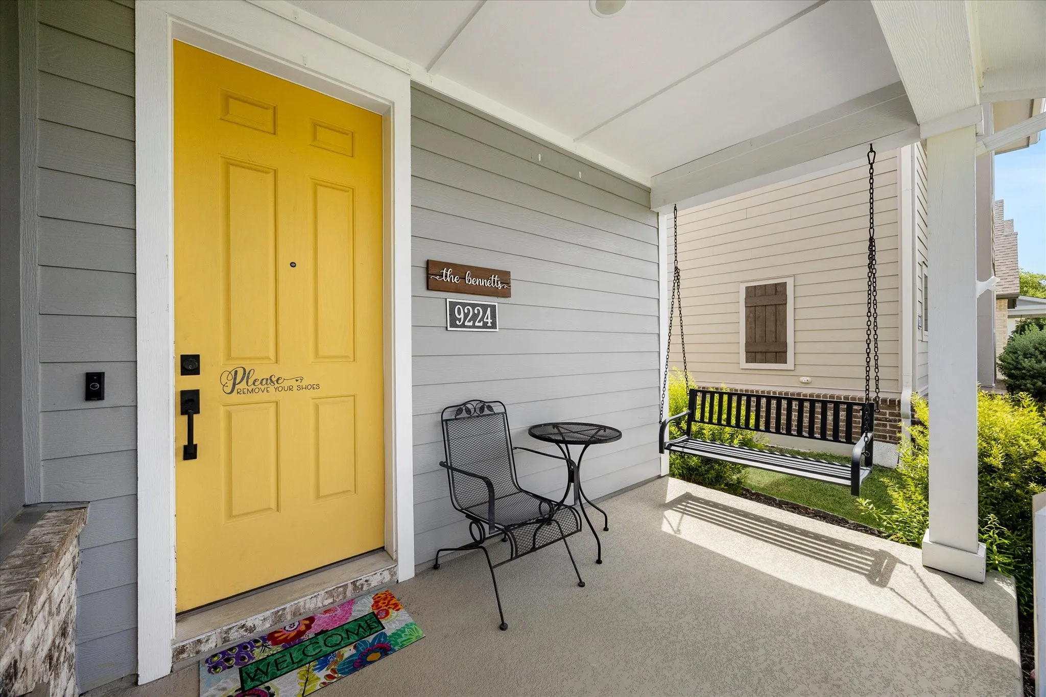 Inviting covered porch featuring grey siding and a vibrant yellow entry door